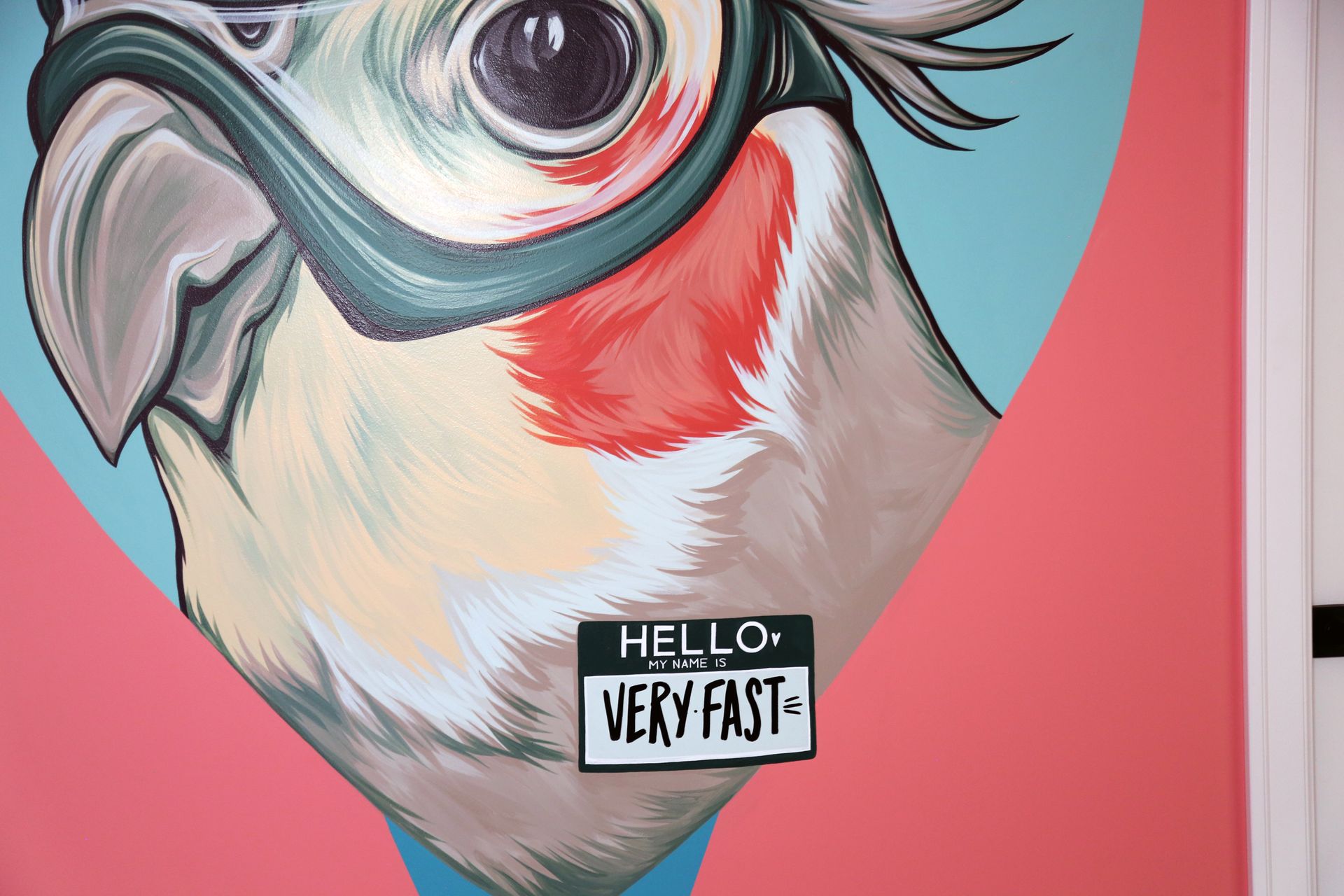 Close-up of a colorful painted bird with a tiny sign reading “HELLO VERY FAST”