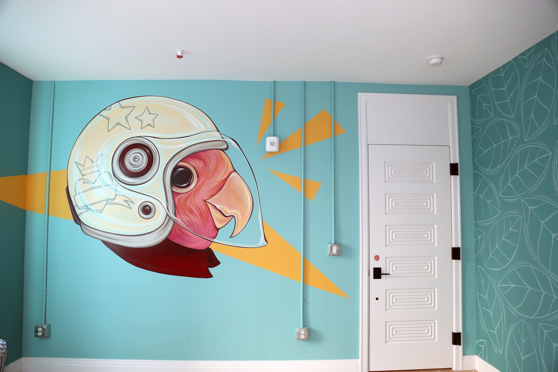 Turquoise room wall mural of a football helmet with orange beams beside a white door