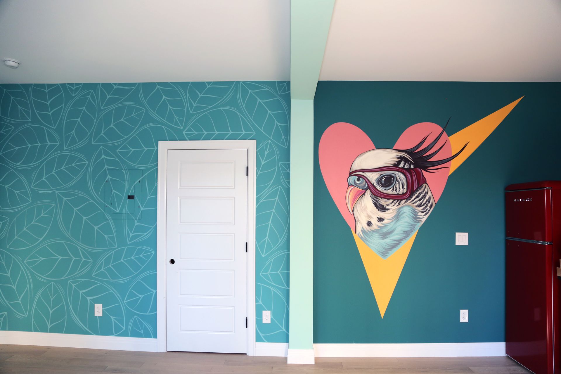 Teal room with a white door and a mural of a dog in goggles and a scarf on the right wall.