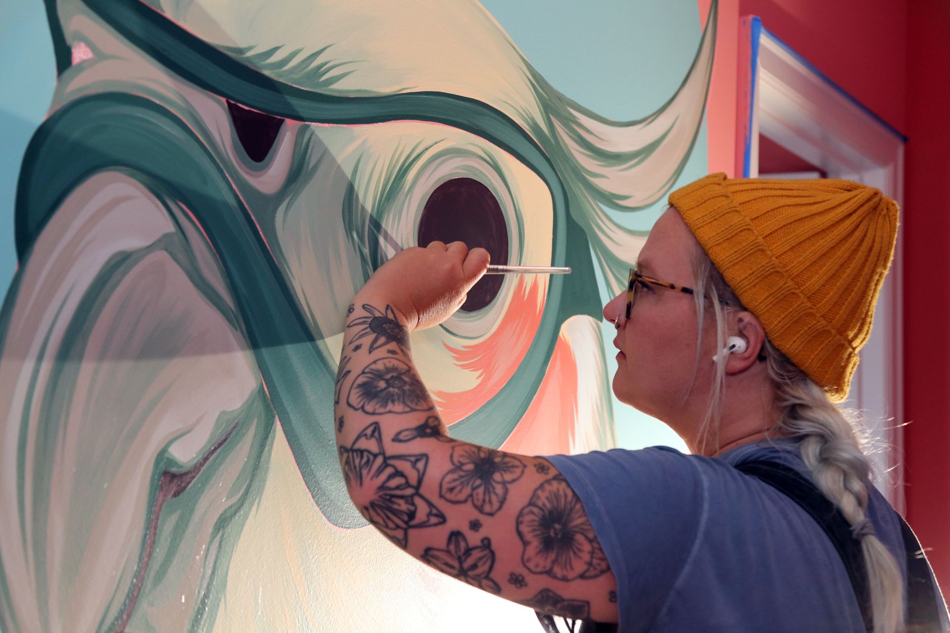 Artist painting a colorful mural on a wall, with teal and pink flowing shapes.