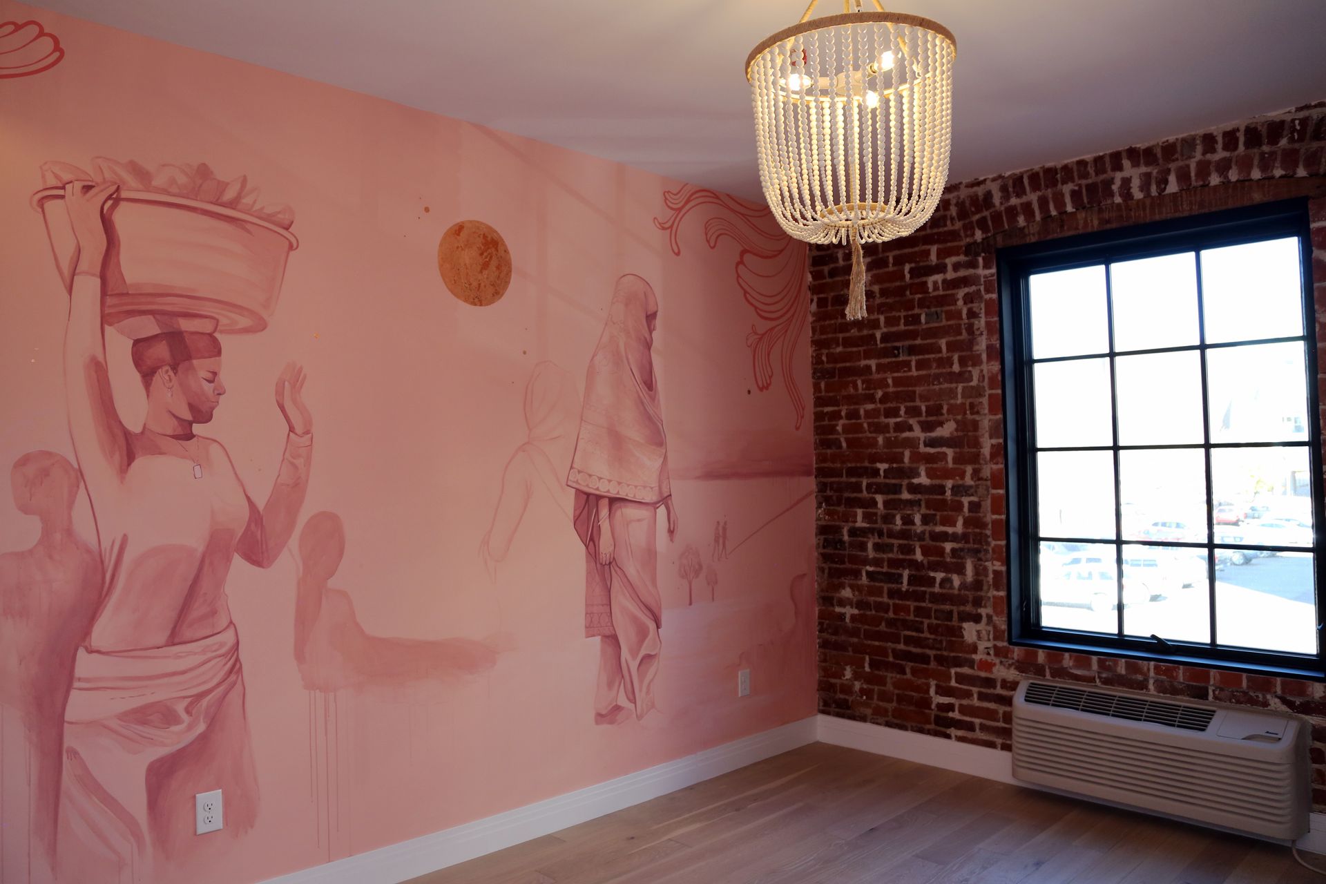 Pink mural-covered room with brick wall, large window, chandelier, and wall radiator.