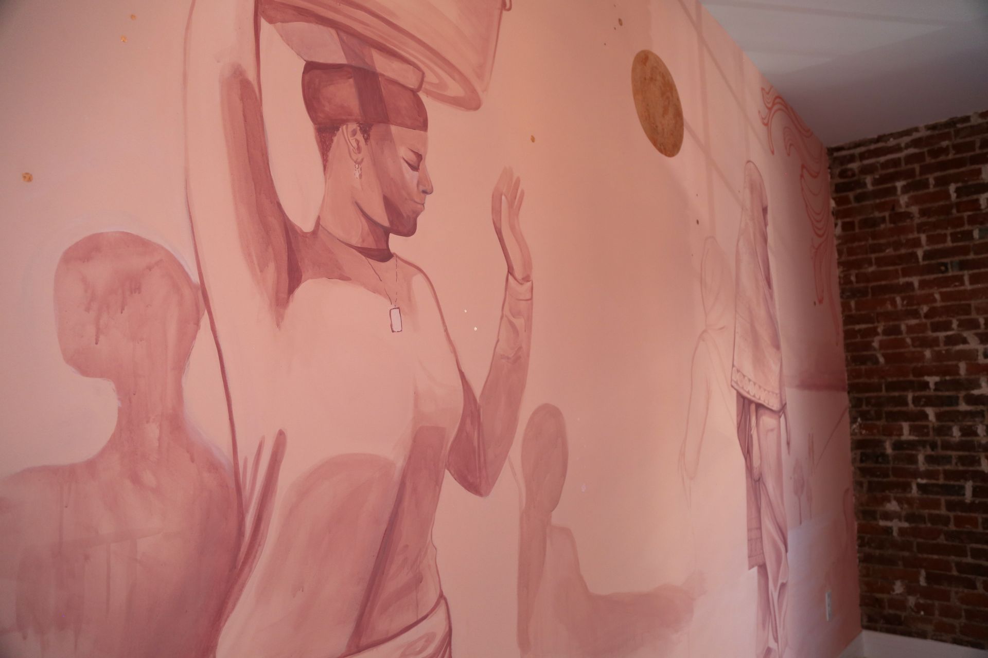 Pink mural of women in hats on a curved wall beside a brick corner and doorway
