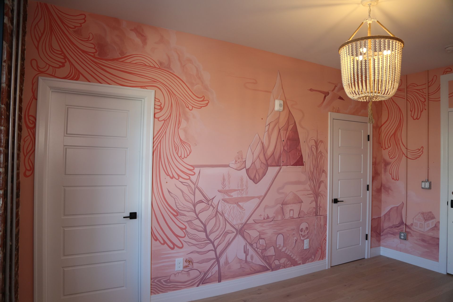 Pink mural-decorated room with two white doors, hardwood floor, and a hanging chandelier