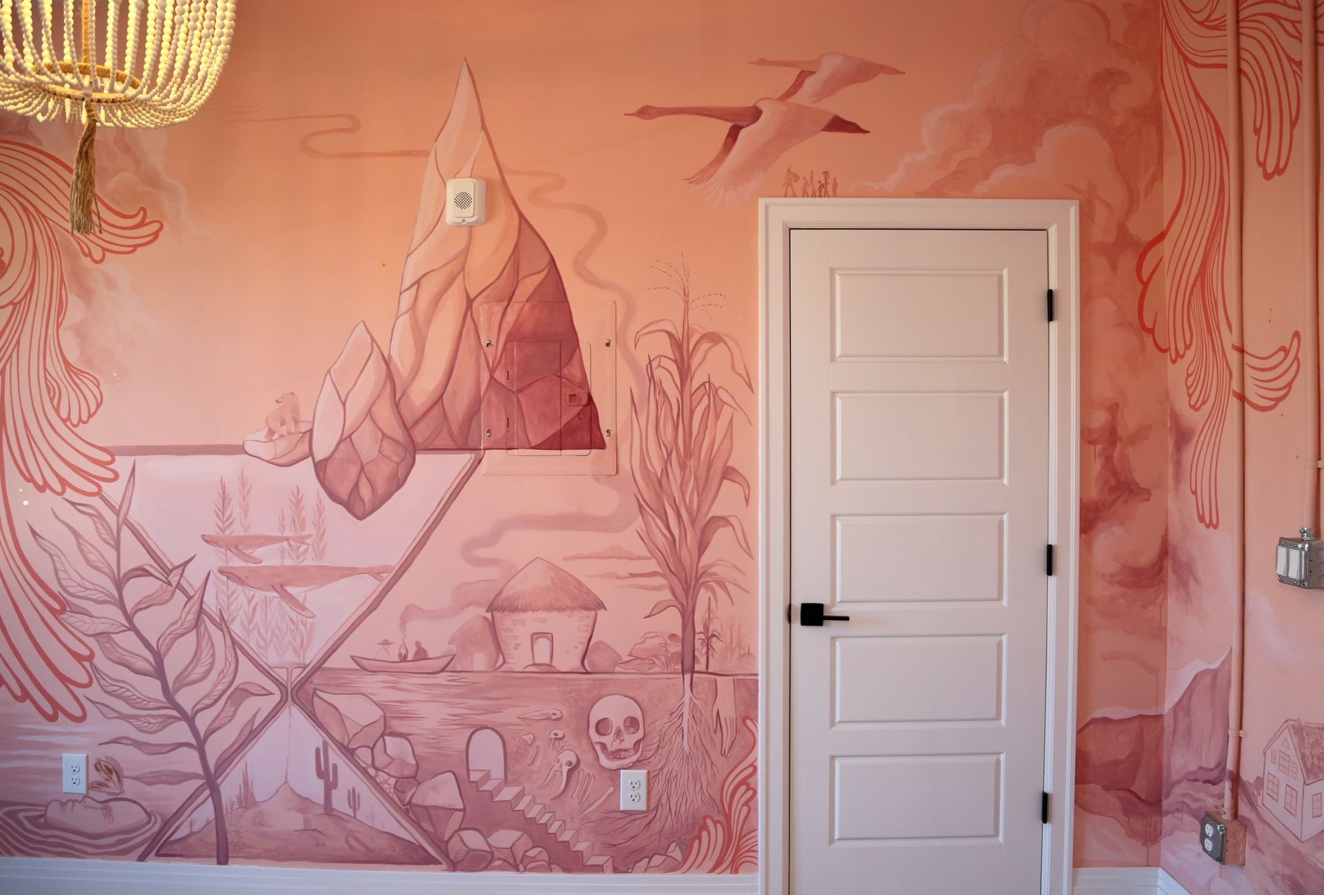 Pink mural wall with mountain, deer, and skeleton drawings beside a white door