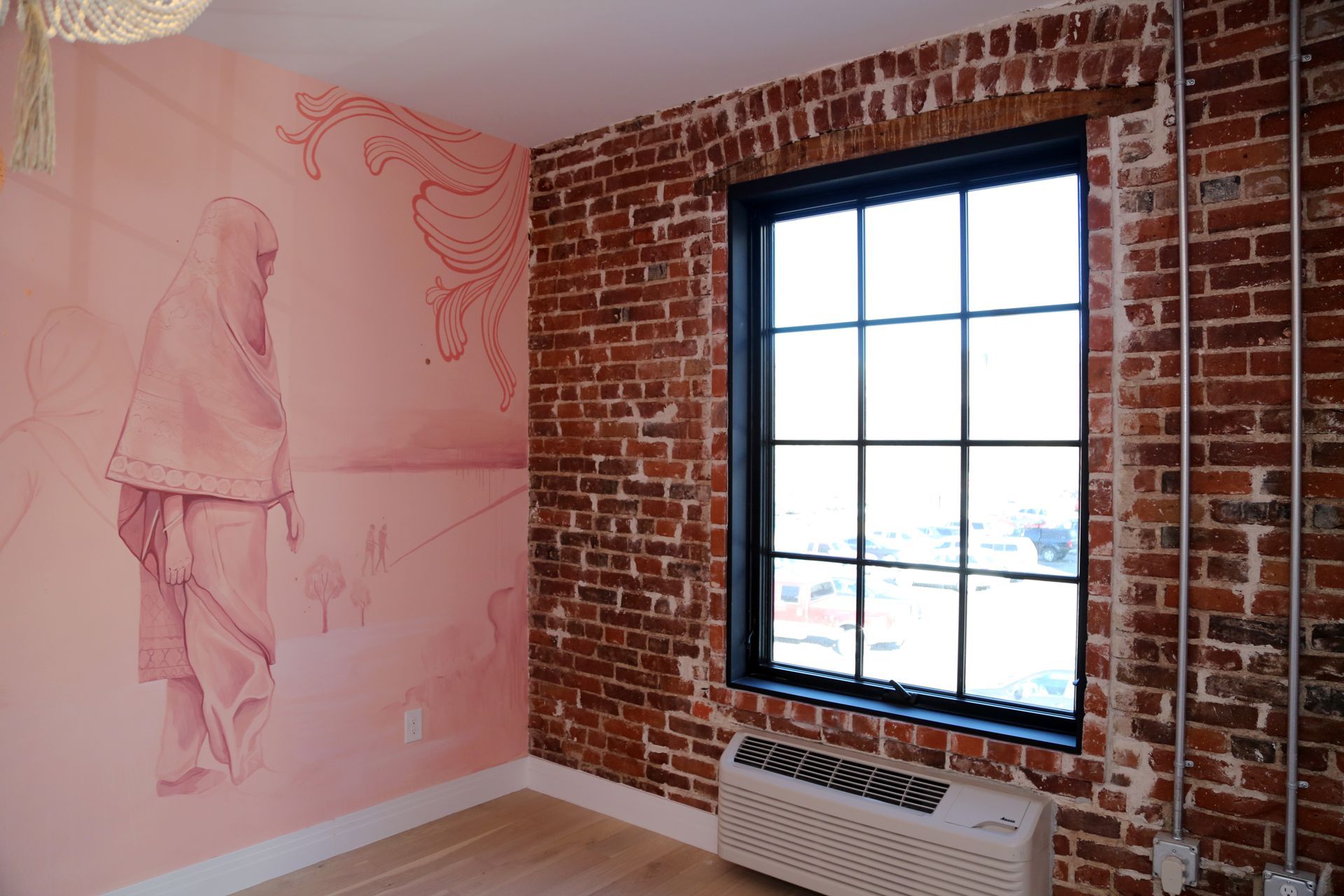 Brick-walled room with a large window and pink mural sketches on the left wall