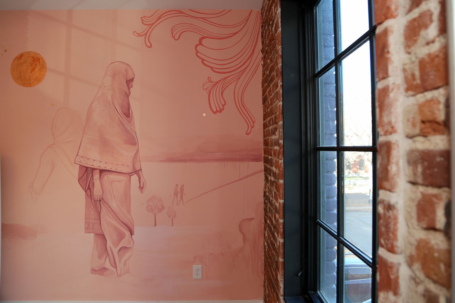 Pink mural on a brick wall beside a window with black metal panes