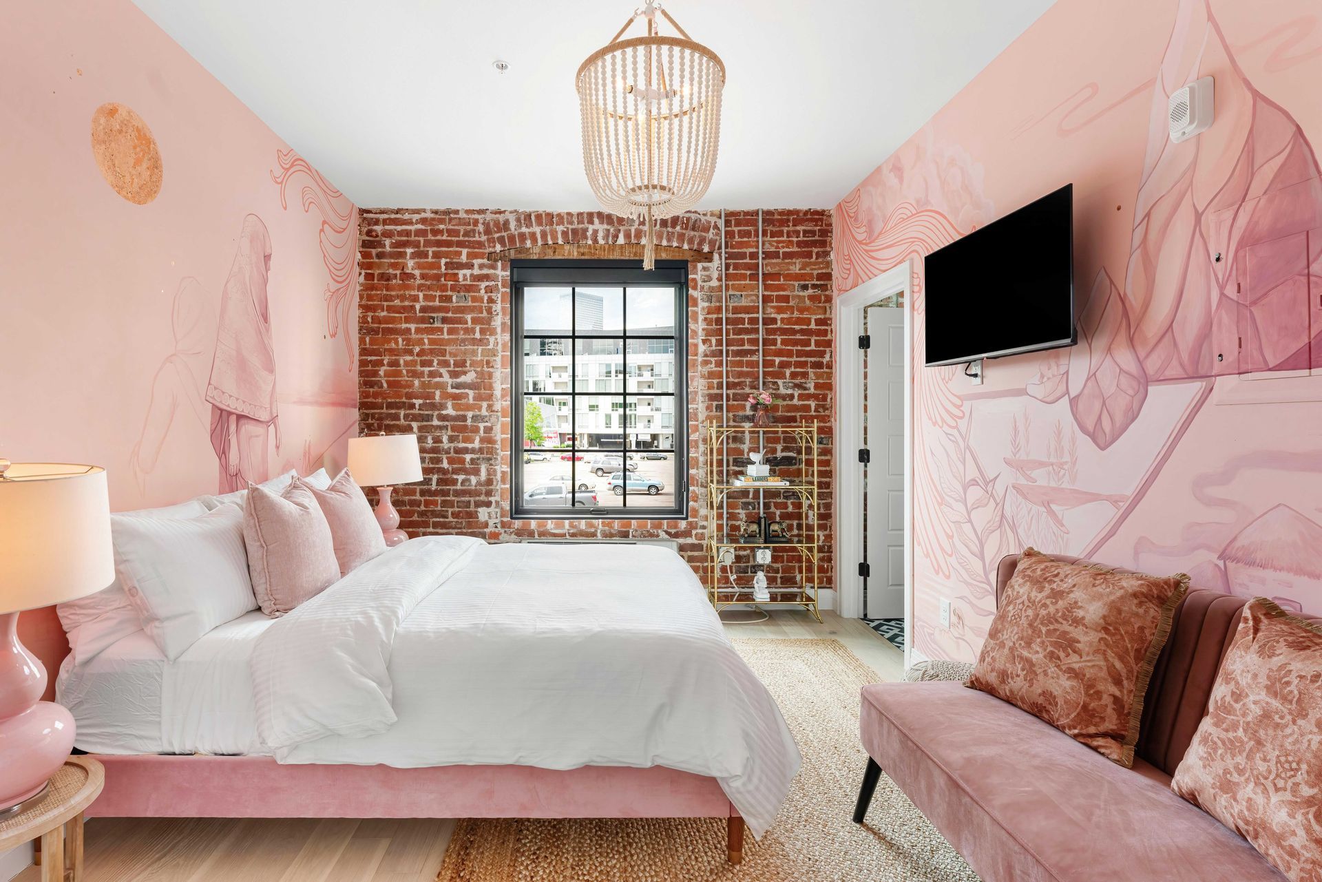 Pink bedroom with exposed brick wall, white bed, and wall-mounted TV