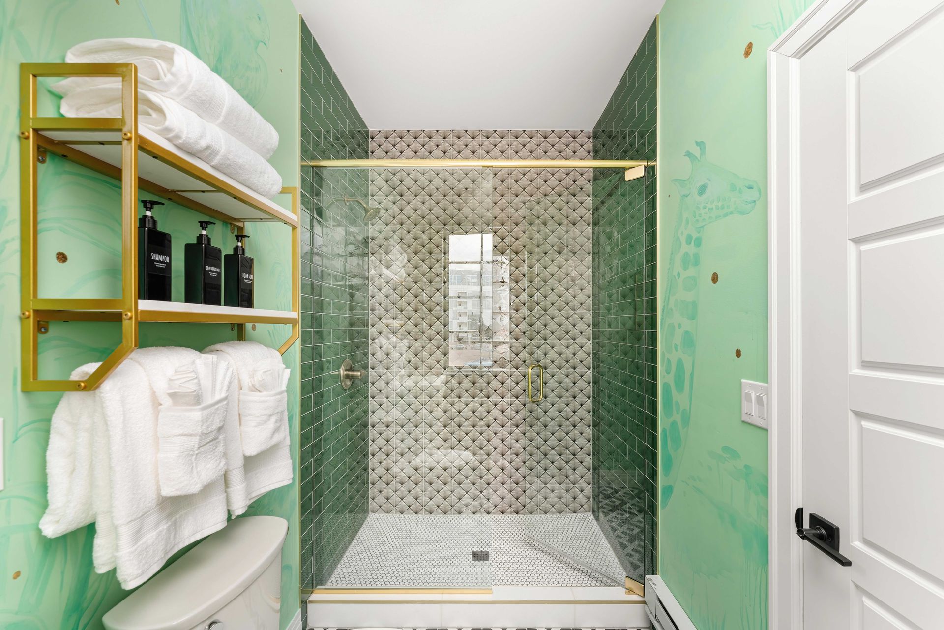 Small mint-green bathroom with glass-tiled shower, white towels, and wall shelf storage