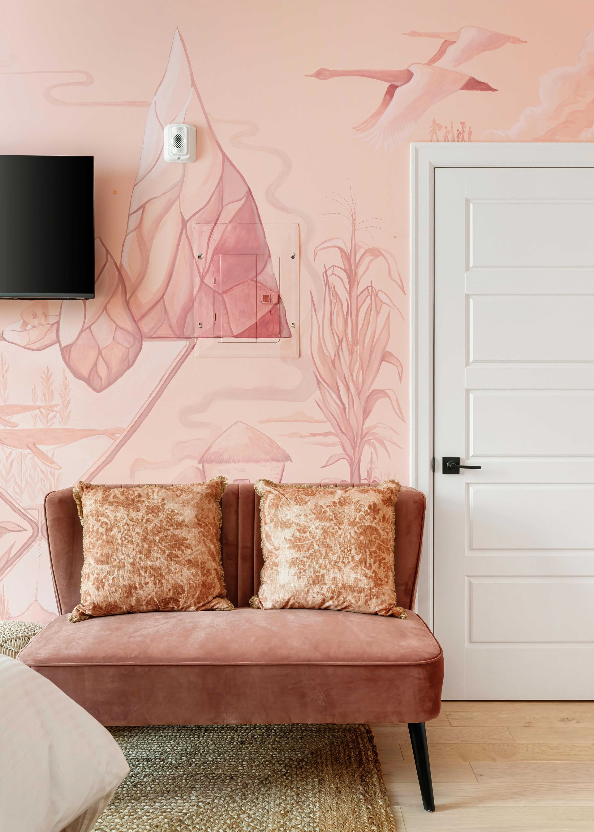 Pink living room with blush wall art, wall-mounted TV, white door, and a rose velvet bench with gold pillows