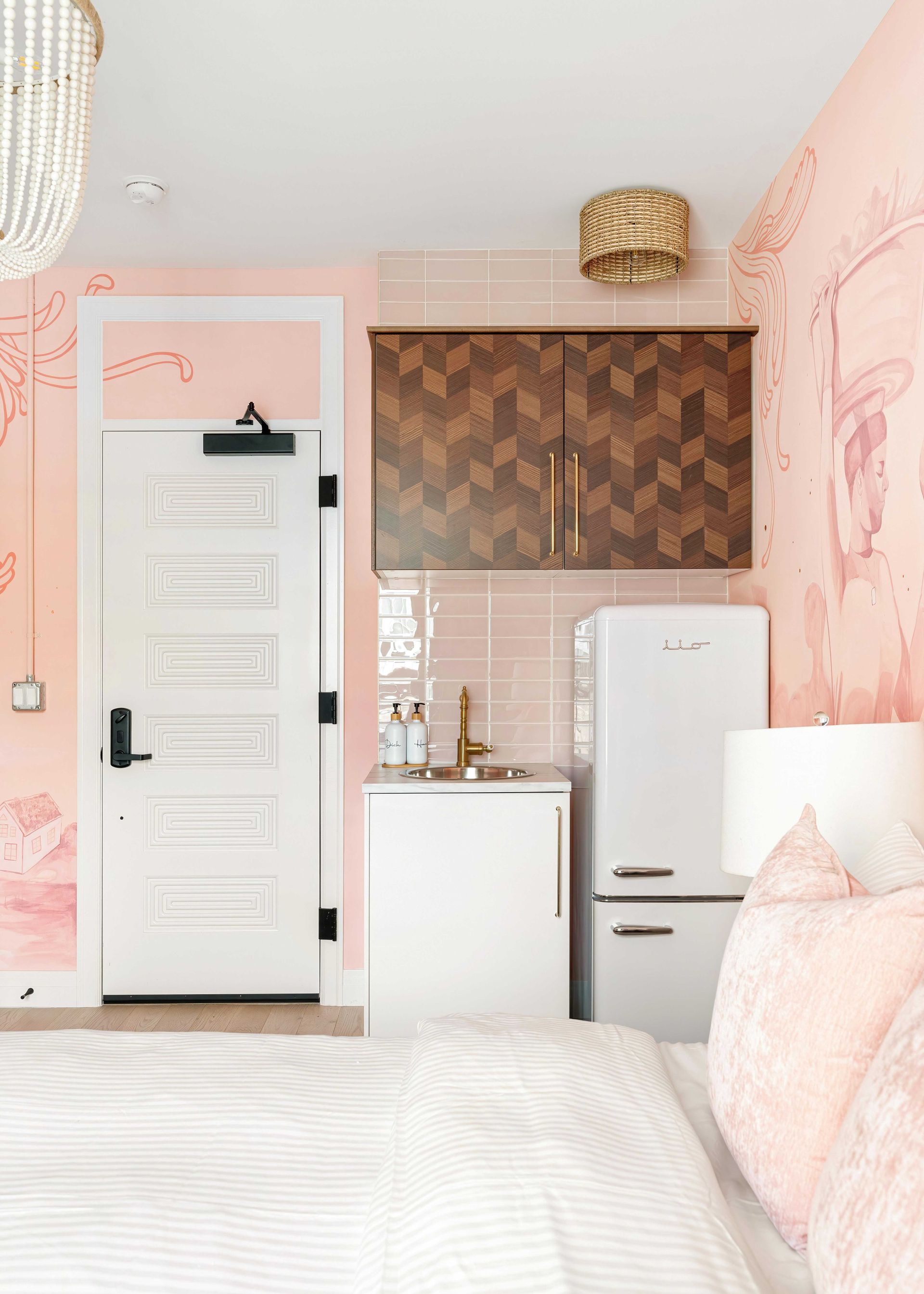 Cozy pink bedroom with a white door, mini kitchen nook, and retro white fridge.