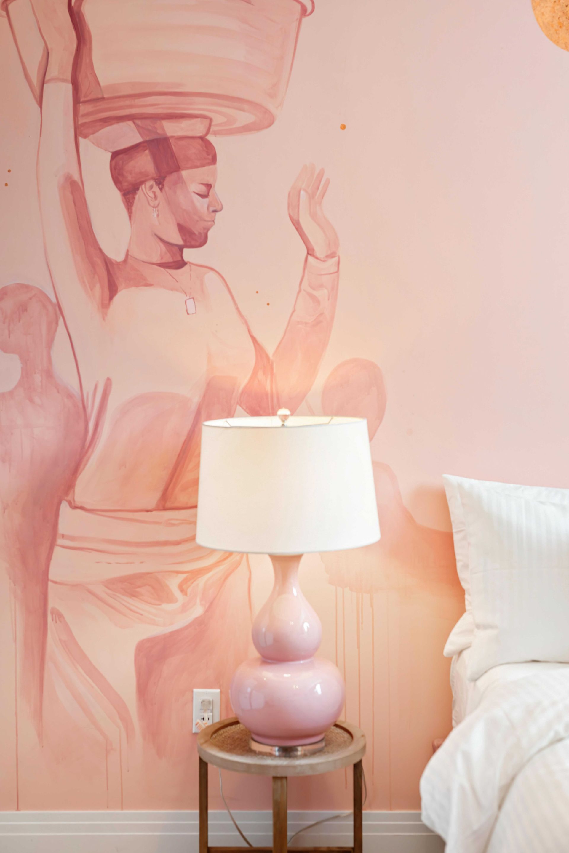 Pink bedroom wall mural beside a bedside lamp and chair, with a white bed and pillow.