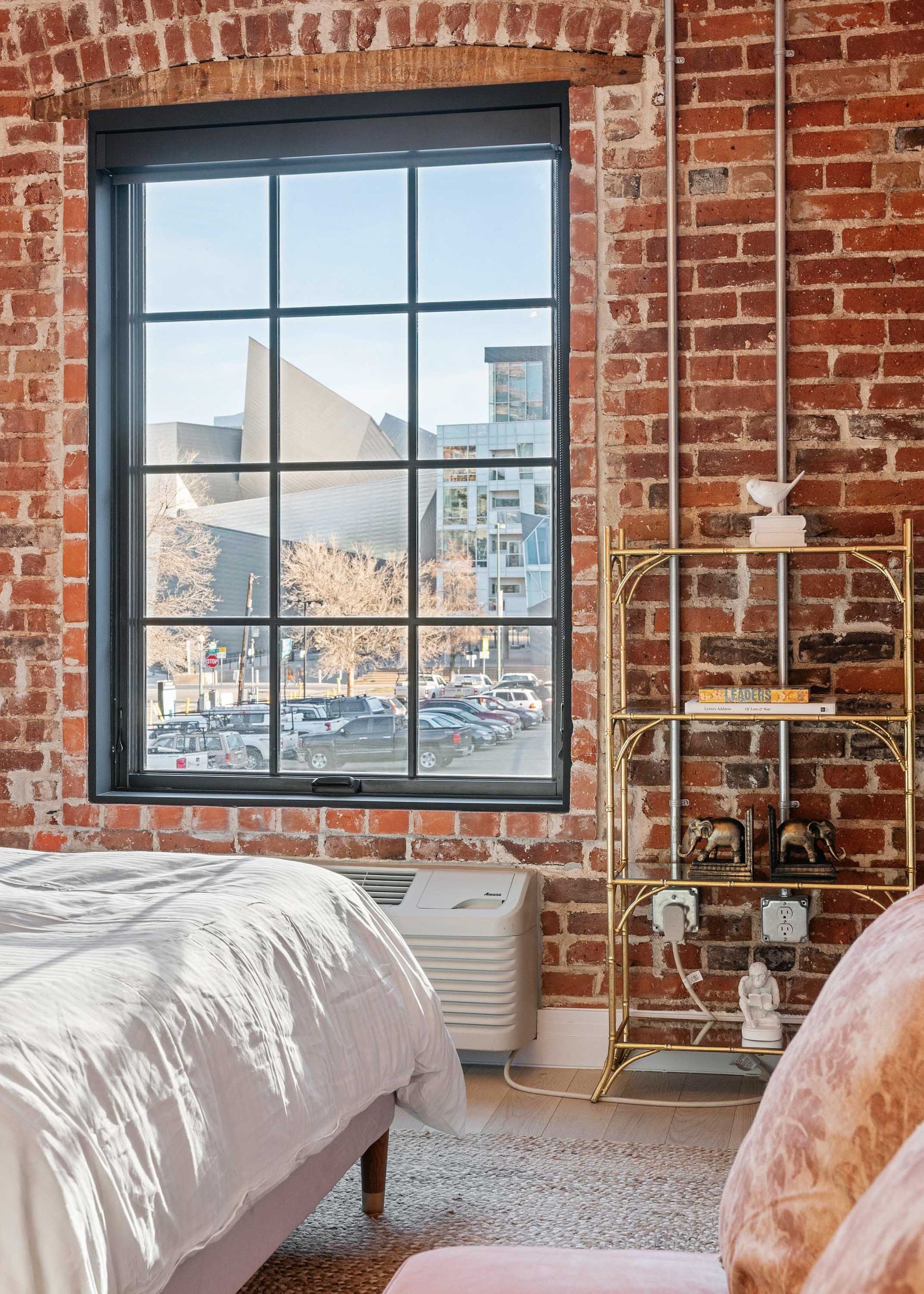 Brick loft bedroom with large window overlooking a cityscape and mountains