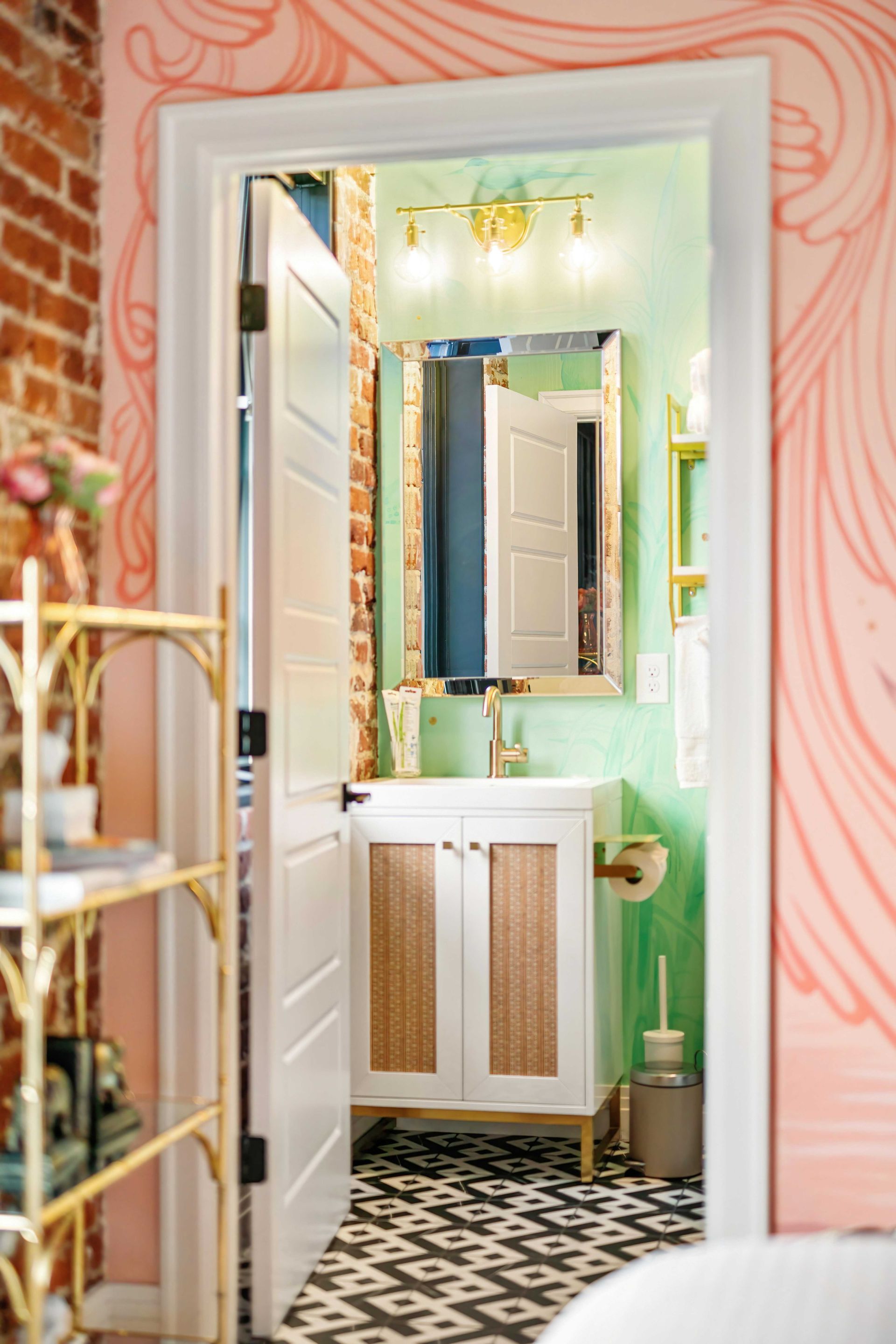 Bathroom vanity with mirror, white cabinet, green walls, and pink swirled wallpaper.