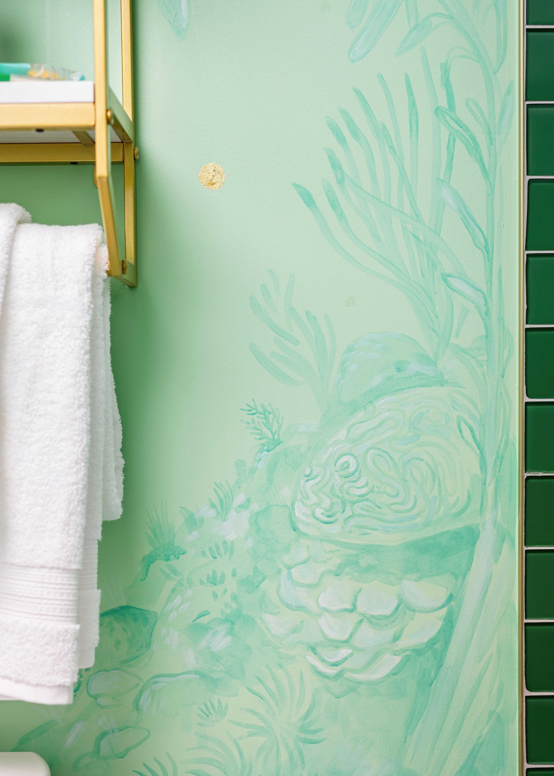 Green bathroom wall with a painted fish and towel rack holding white towels