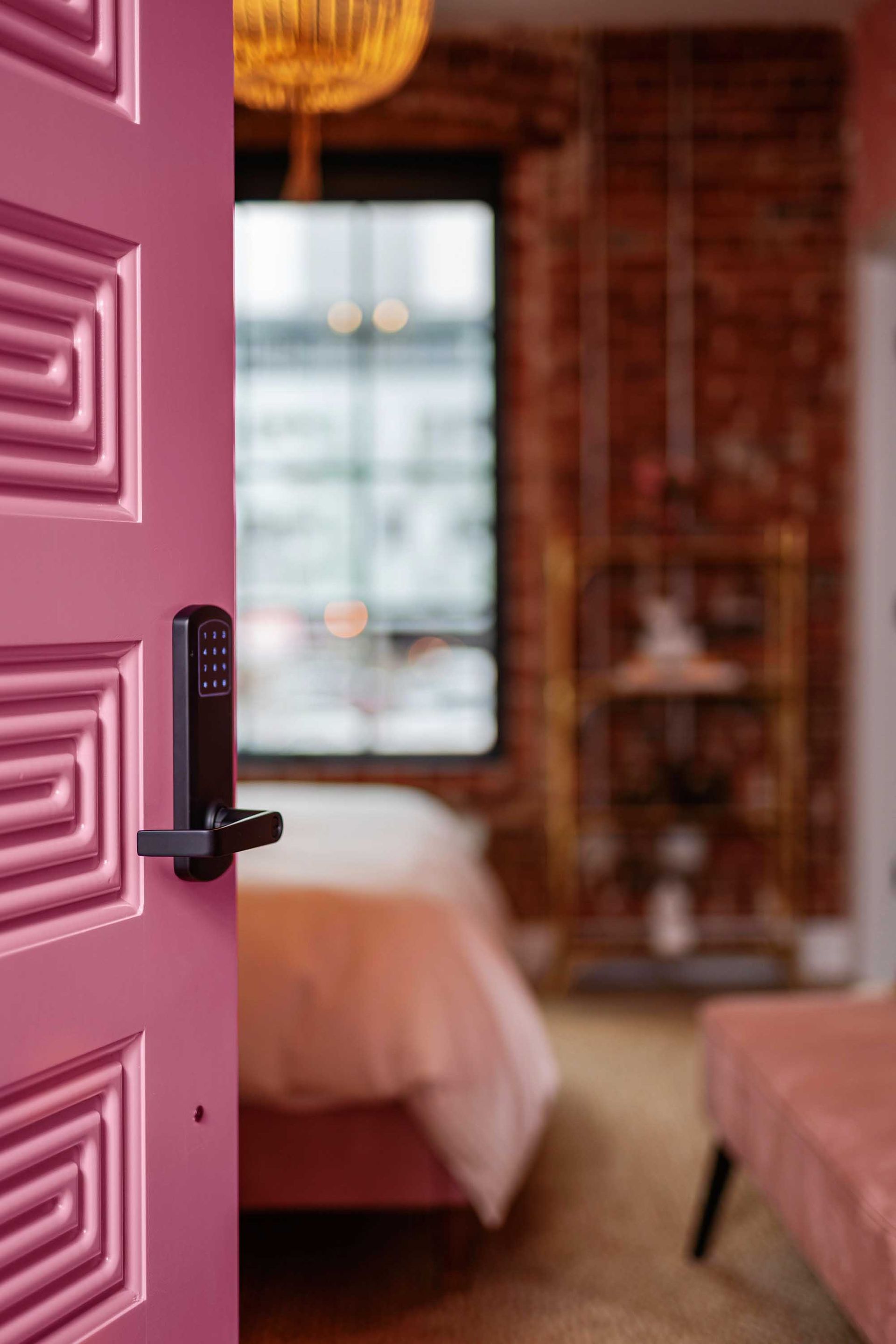 Open pink door framing a cozy bedroom with brick walls and a window