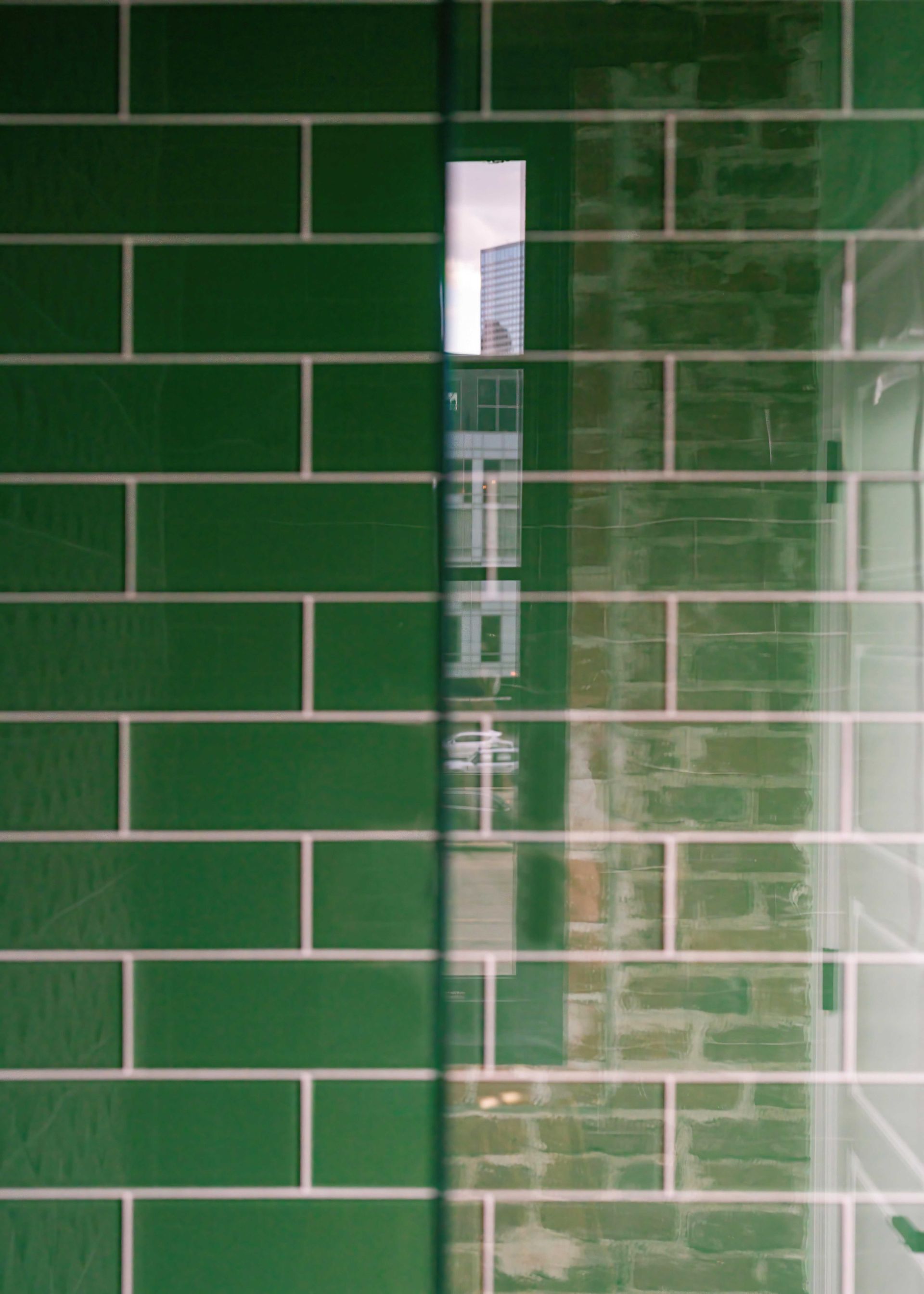 Green tiled wall with a narrow vertical glass window or opening in the center.
