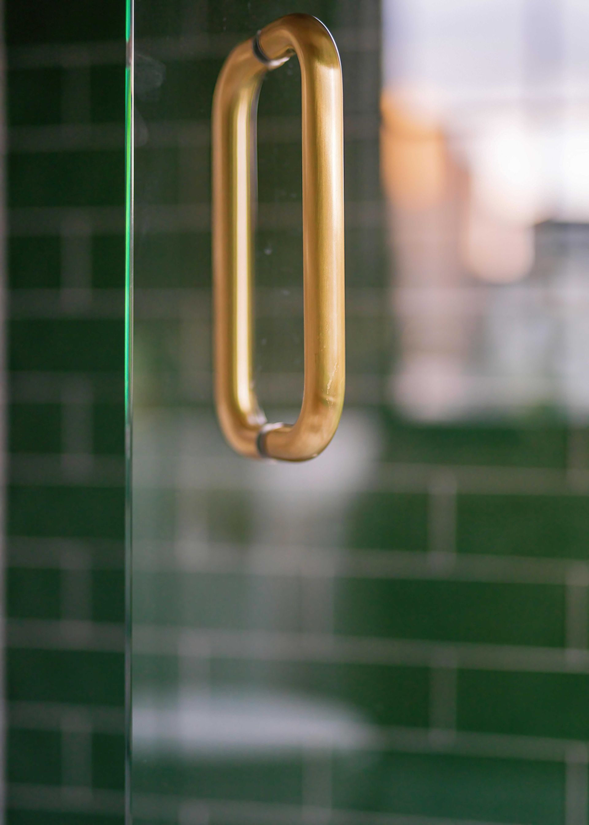 Gold door handle on a glass door with green tiled background