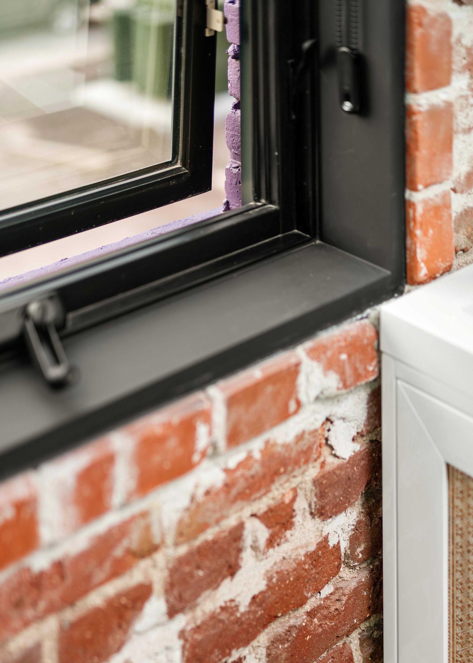 Close-up of a black window frame against a red brick wall and white trim