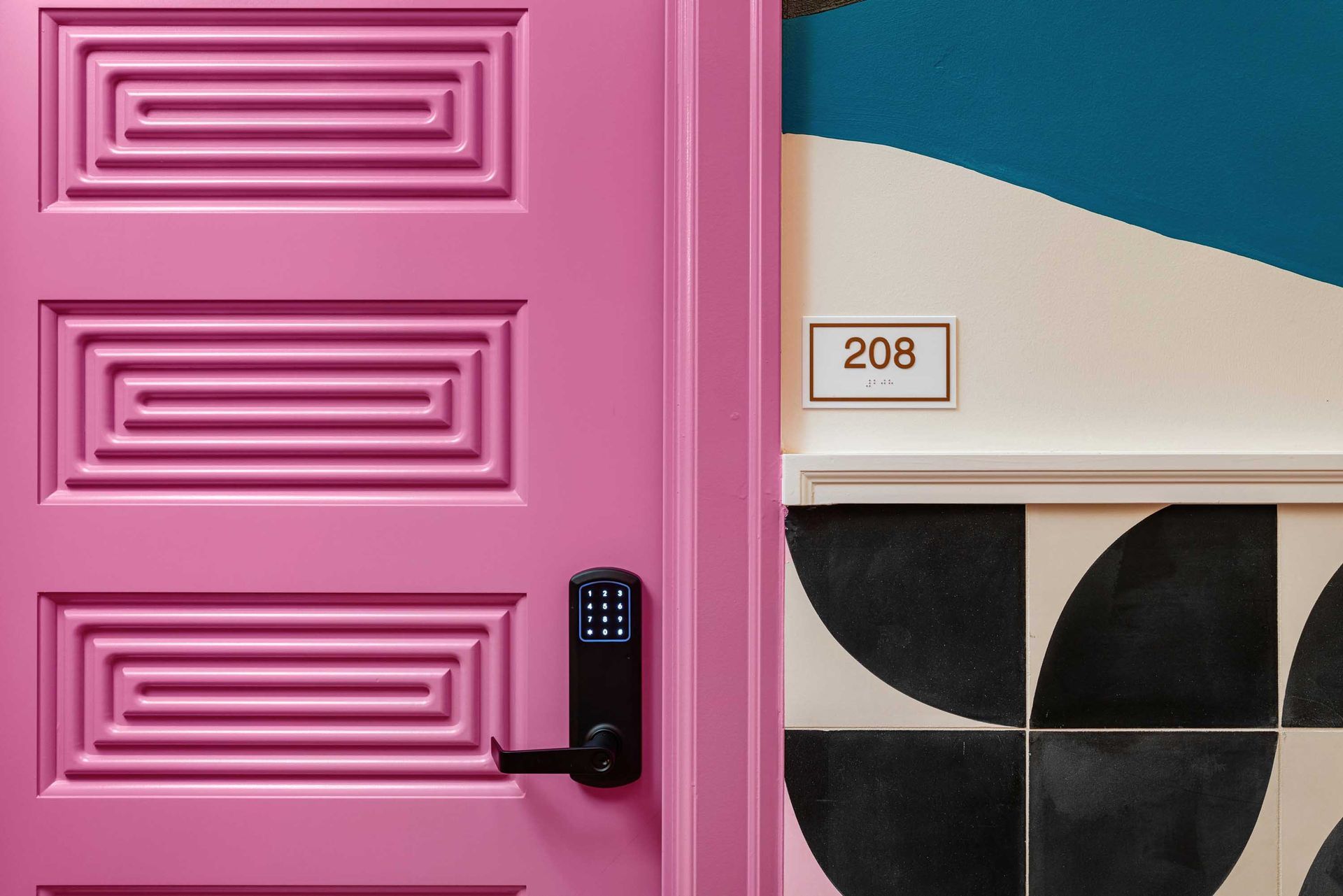 Pink door with keypad lock next to a room number 208 sign and black-and-white geometric wall tiles
