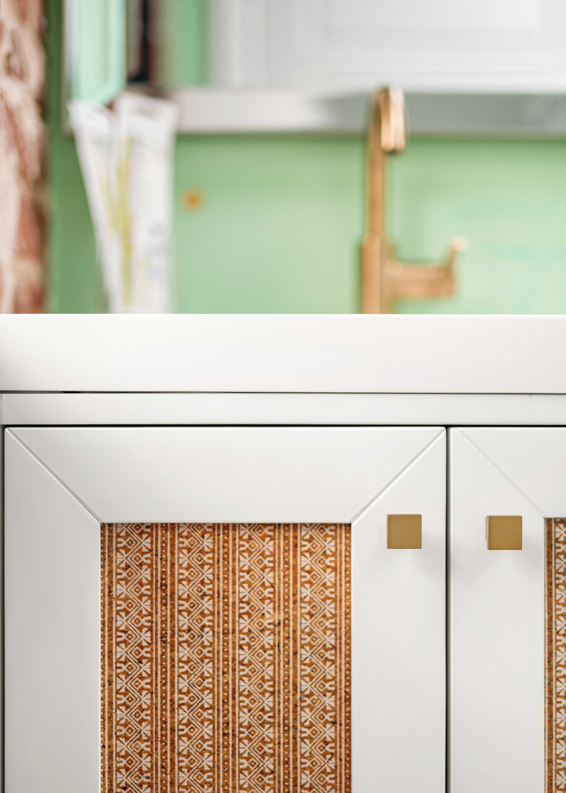 White cabinet with woven brown panel and brass handles in a soft green room interior