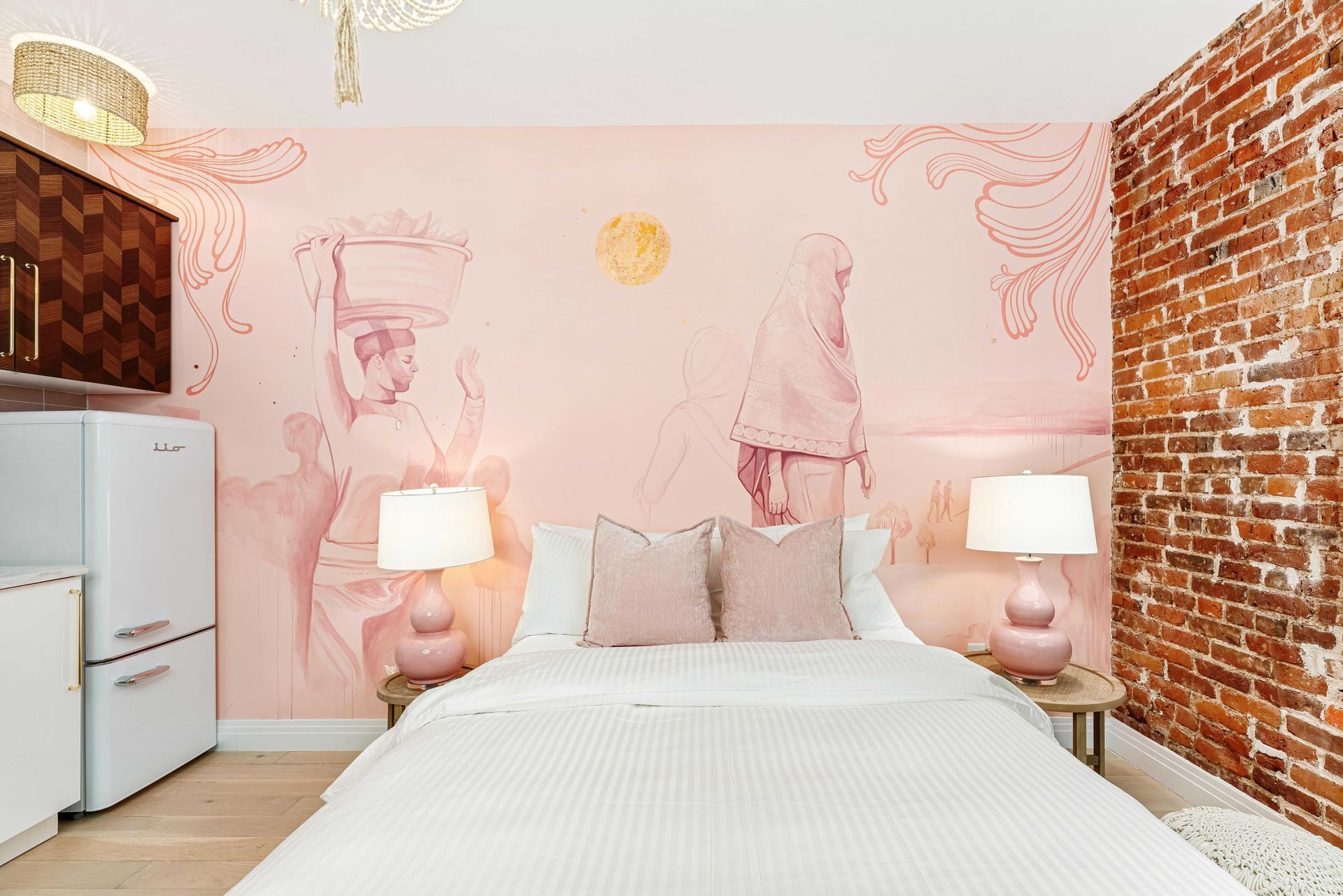 Pink bedroom with twin beds, exposed brick walls, and white lamps on bedside tables