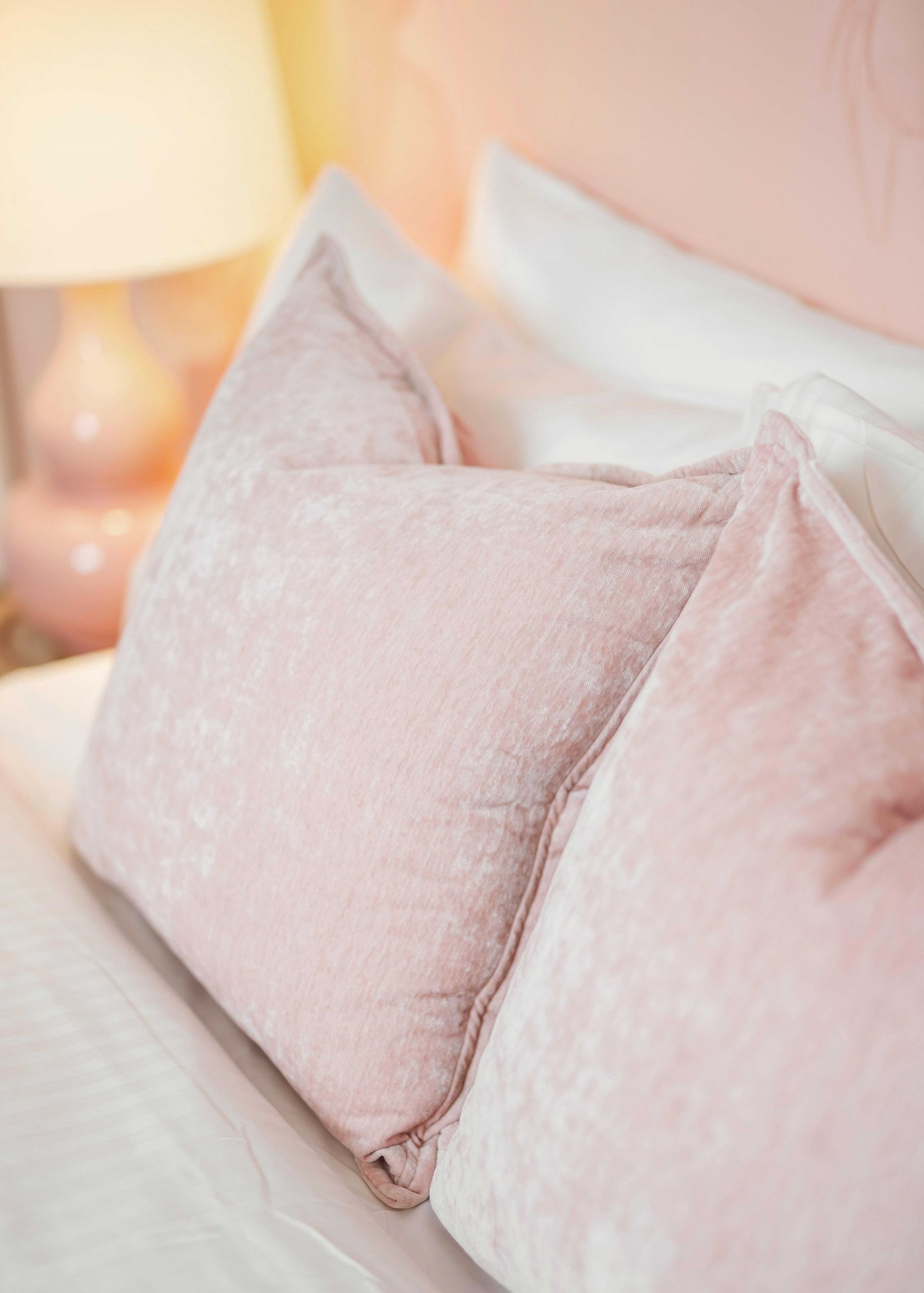 Pink textured pillows on a bed beside a glowing bedside lamp