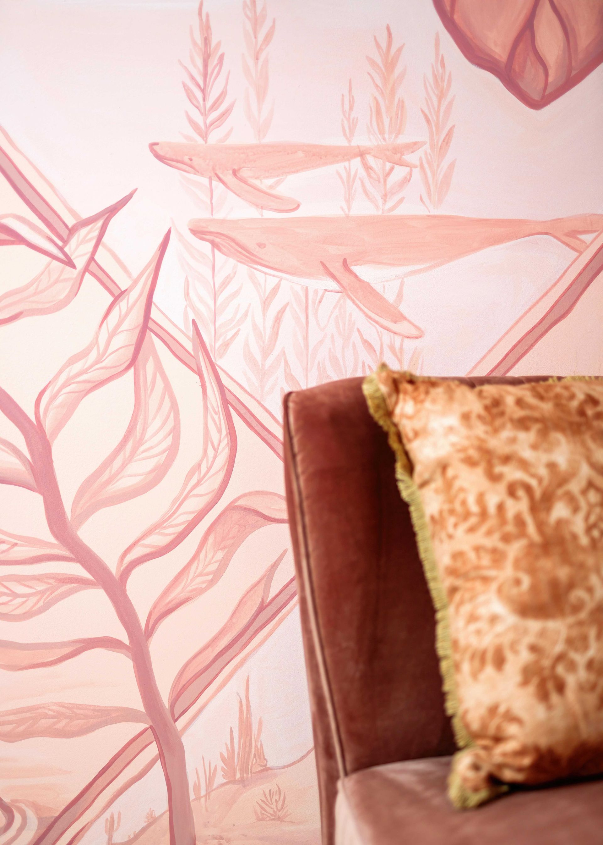 Pink leaf-pattern wallpaper behind a brown sofa with a beige patterned pillow.