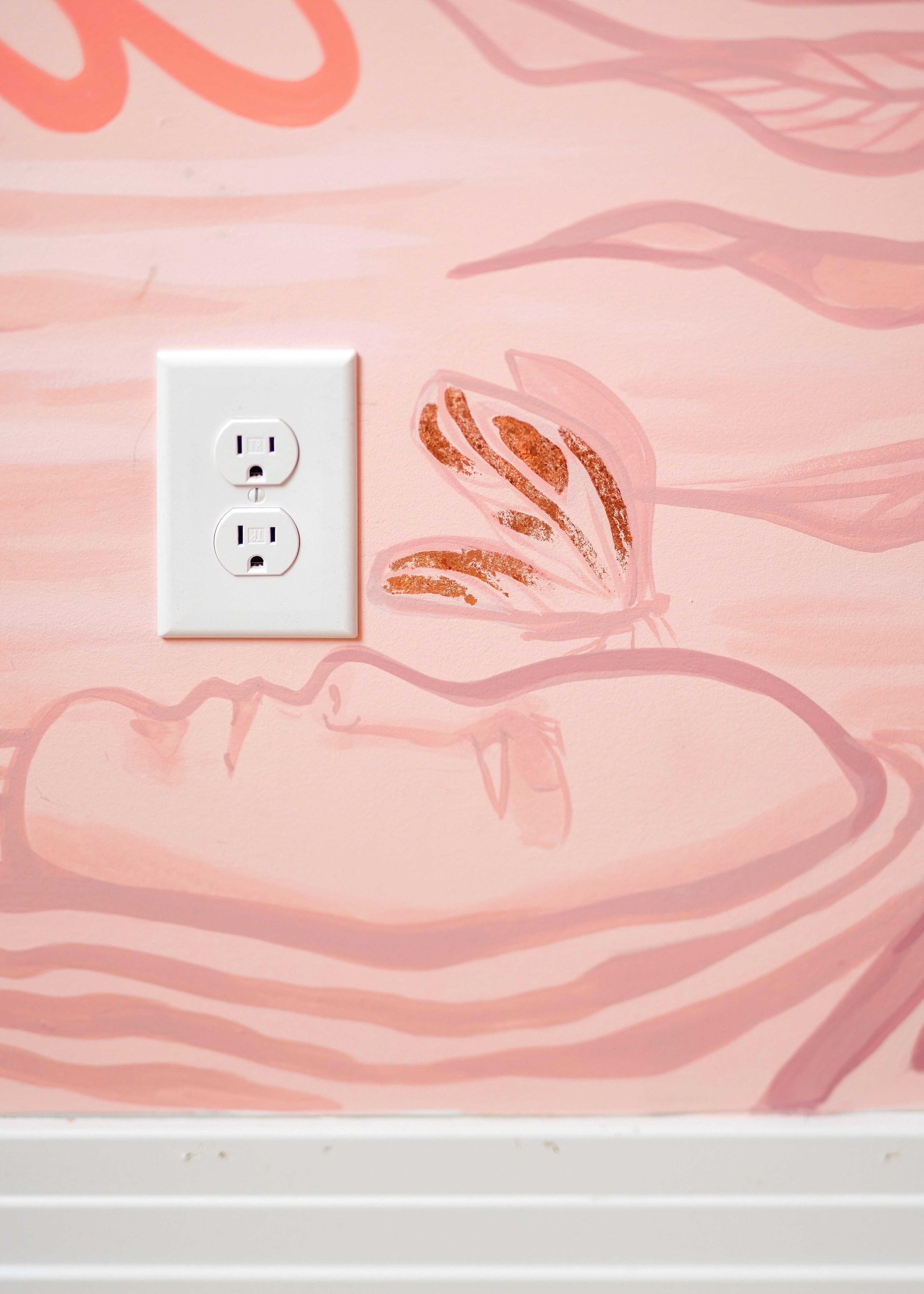 Pink patterned wall with a white electrical outlet and white baseboard