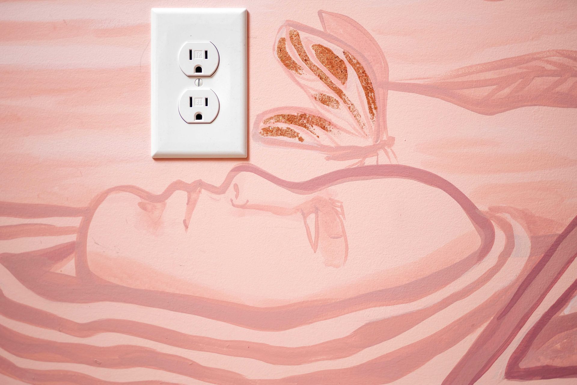Pink mural of a sleeping face with a butterfly and a white electrical outlet on the wall