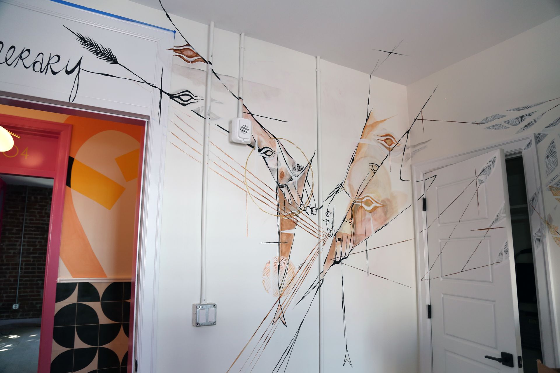 White room wall with large abstract branch-and-line mural, open doorways, and colorful orange-red adjoining room.
