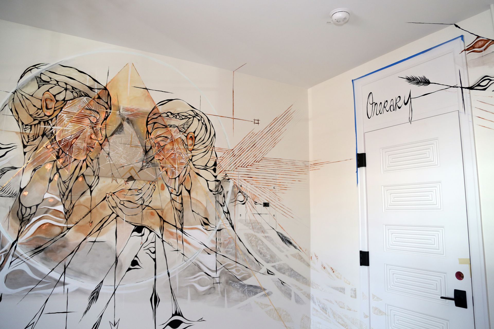 Mural of two abstract figures on a white wall beside a white door in a bright room
