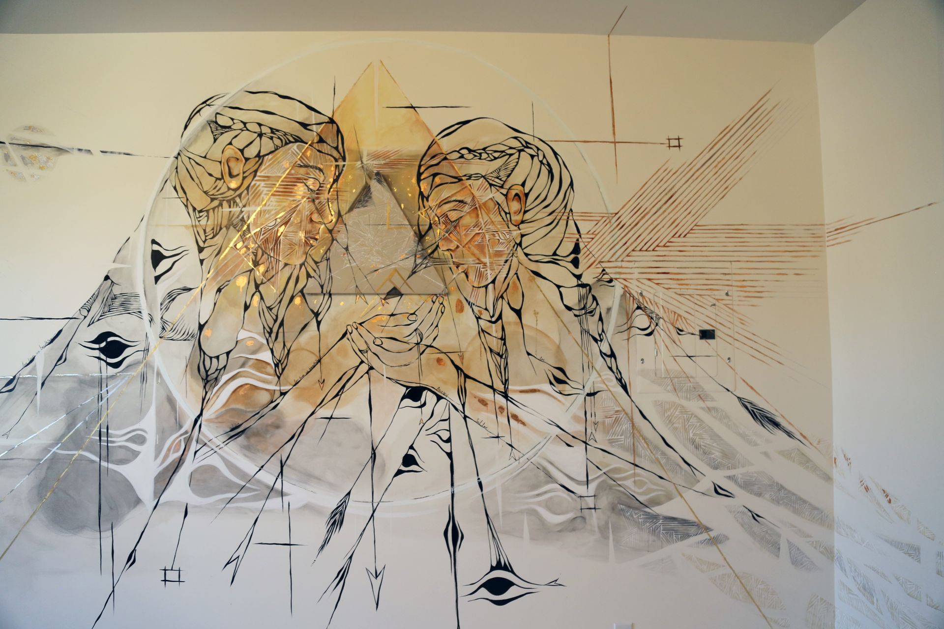 Abstract wall mural with overlapping black, white, gray, and gold geometric lines and figures