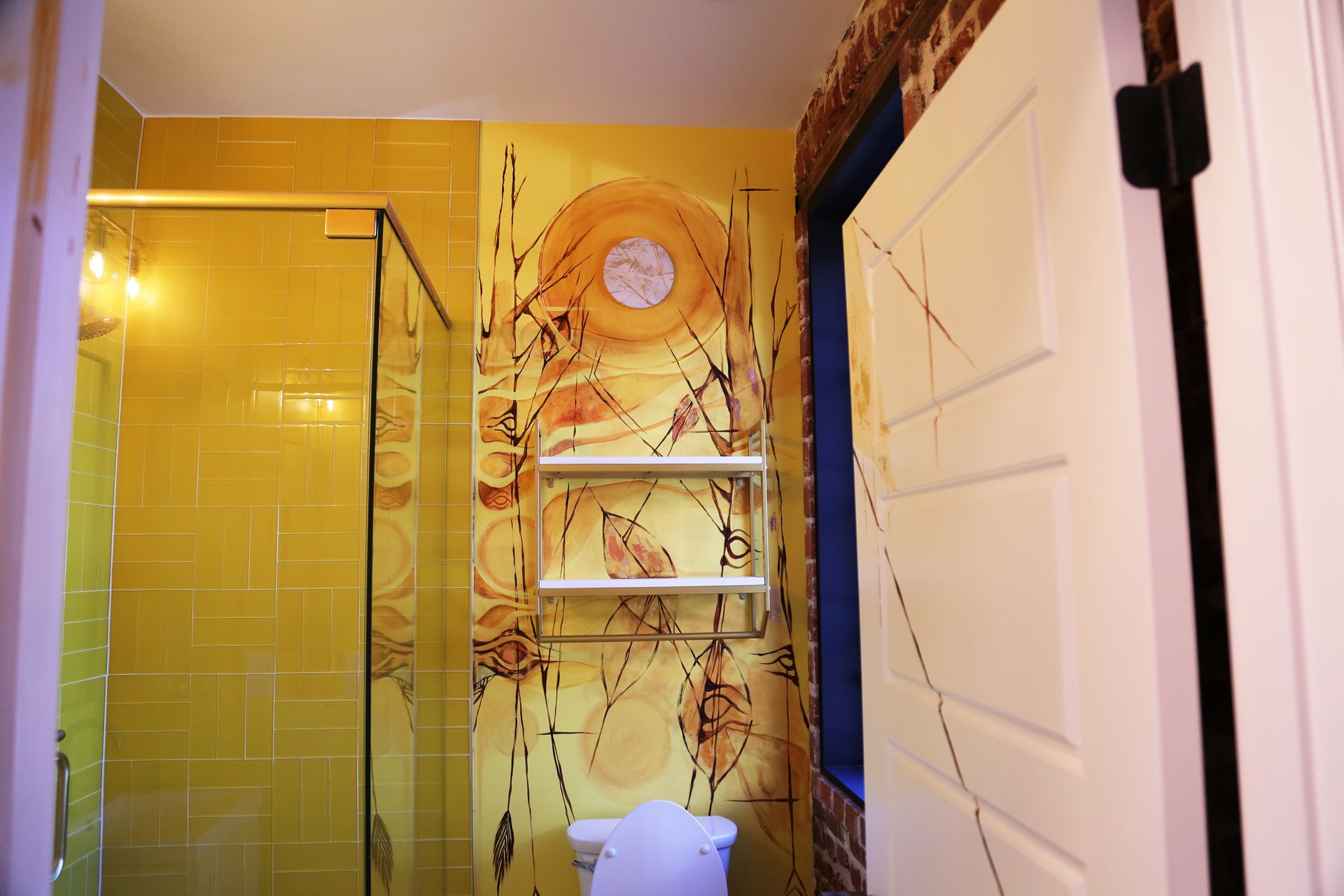 Bathroom with yellow shower doors, white shelving, and a decorative wall hanging above a toilet.