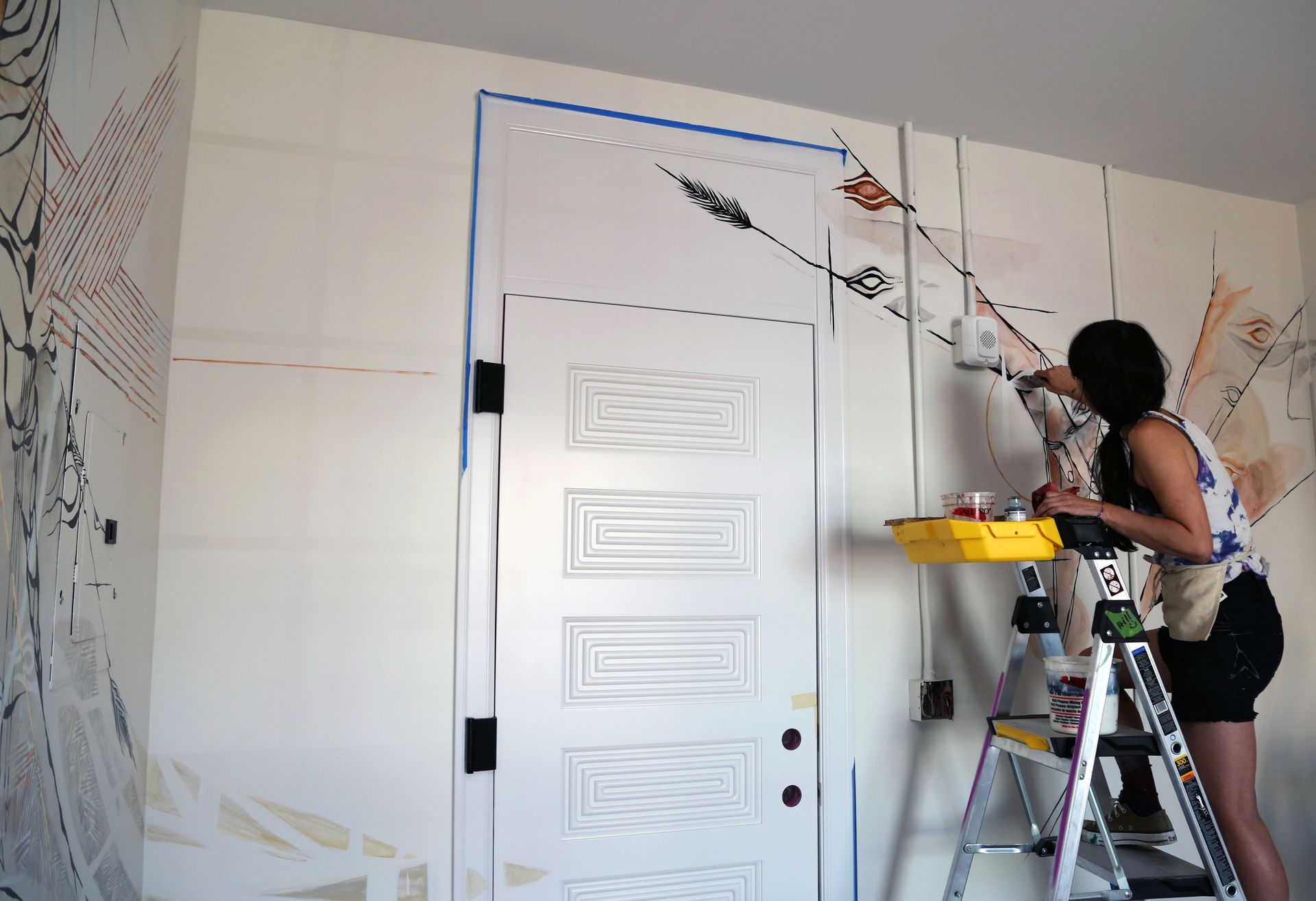 Person painting a white wall above a door using a roller on an extension pole.