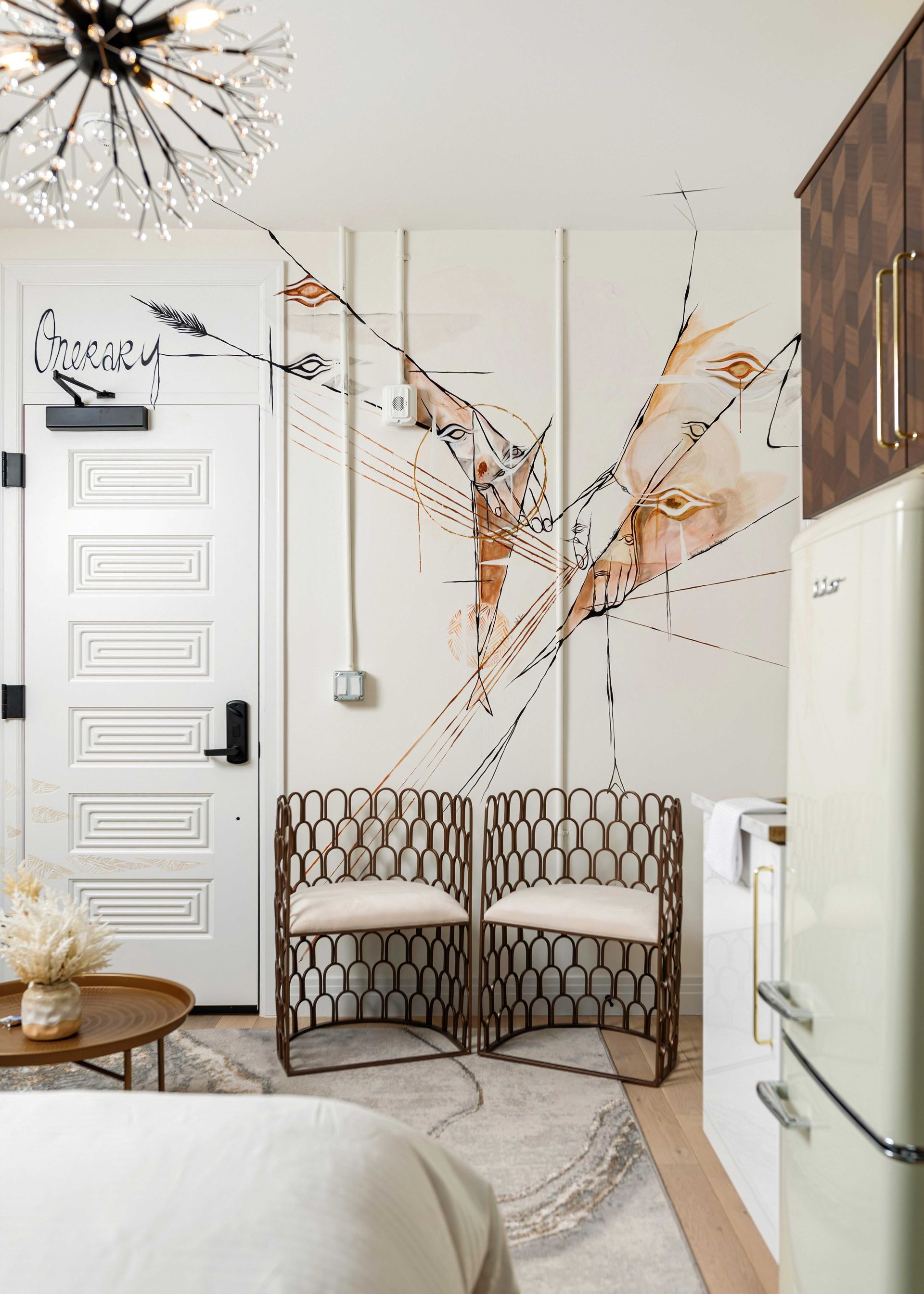 Modern entryway with patterned chairs, white door, mural wall art, and a small refrigerator