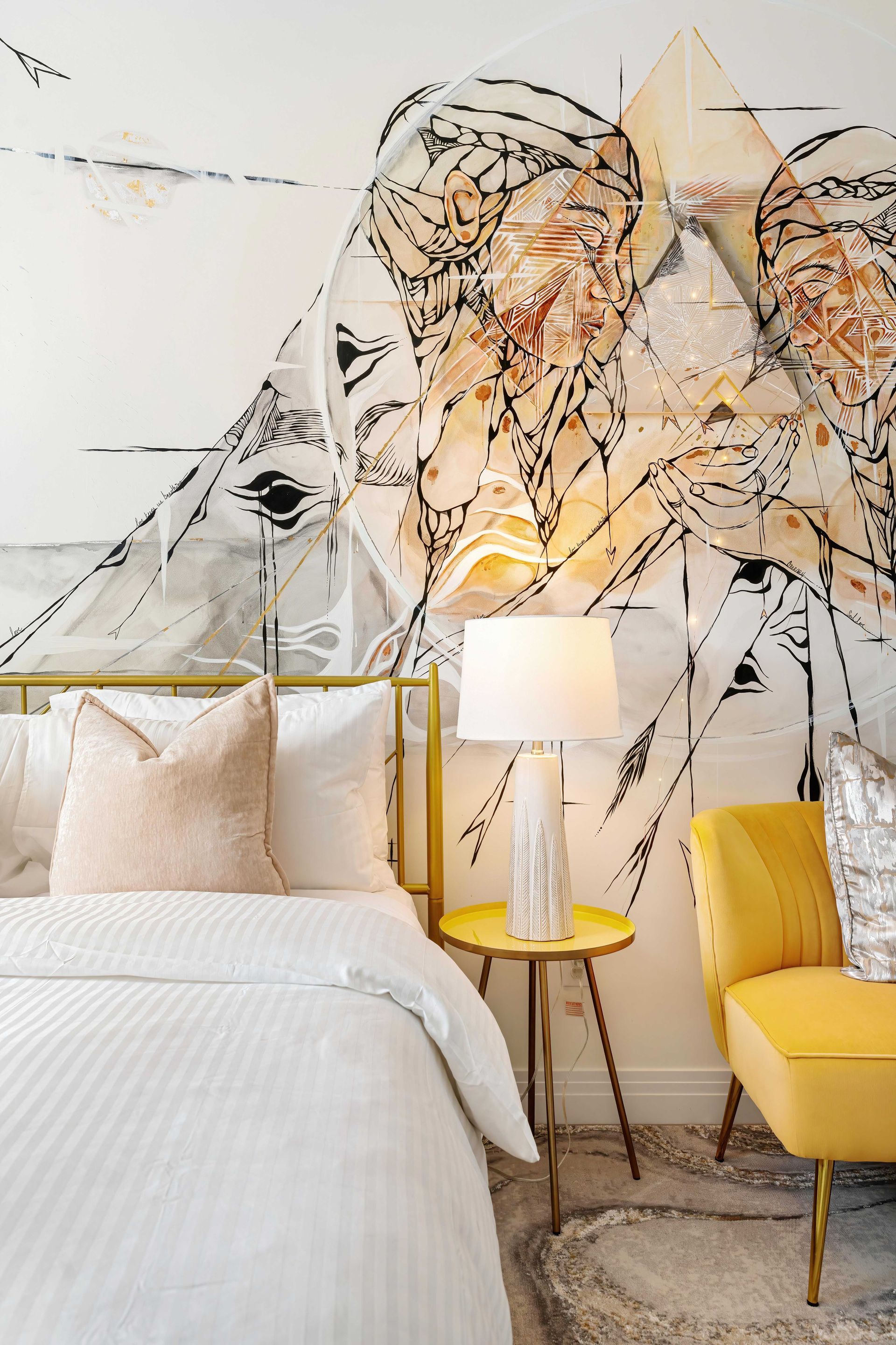 Modern bedroom with white bedding, geometric mural, yellow chair, and gold lamp