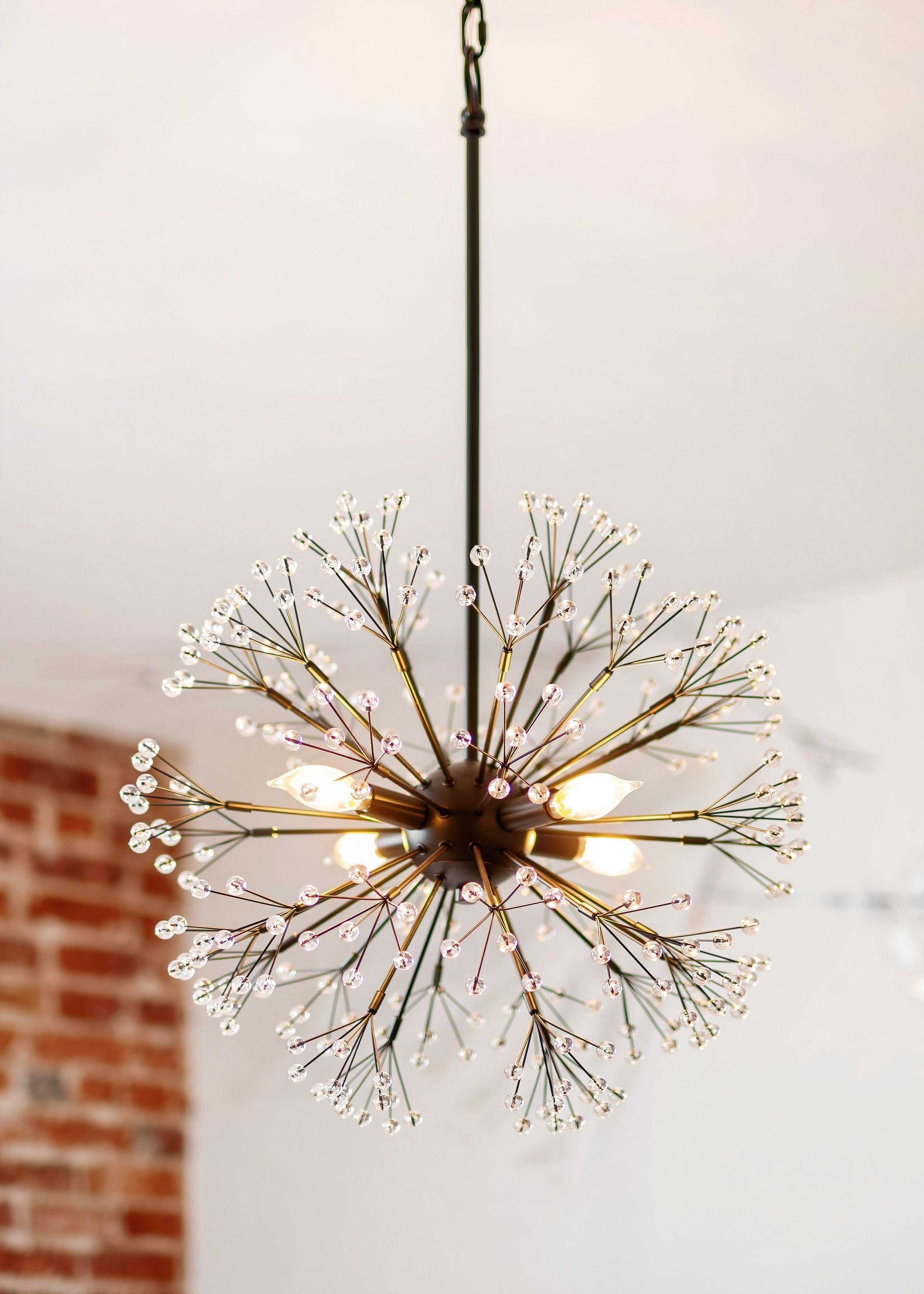 Modern chandelier with white branch-like arms and warm lights hanging from a ceiling near a brick wall