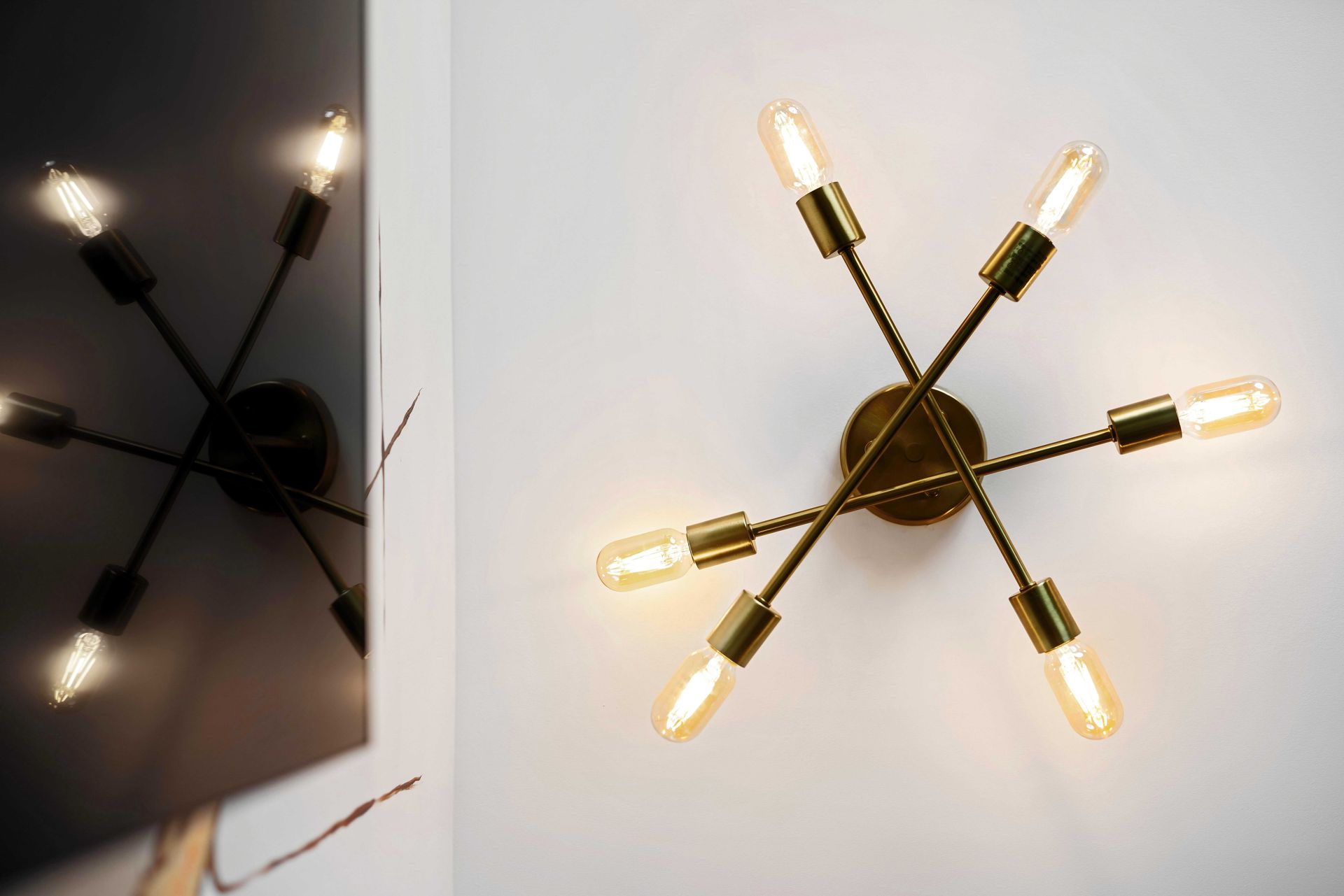 Modern brass starburst wall sconce with six exposed bulbs on a white wall