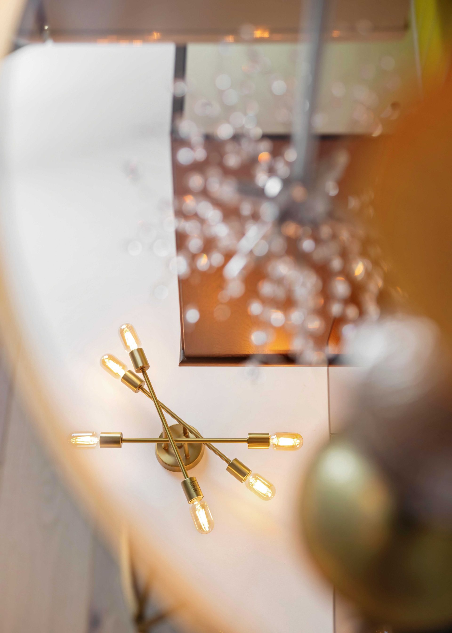 Gold starburst chandelier against a white ceiling, with a blurred hanging ornament in the foreground.
