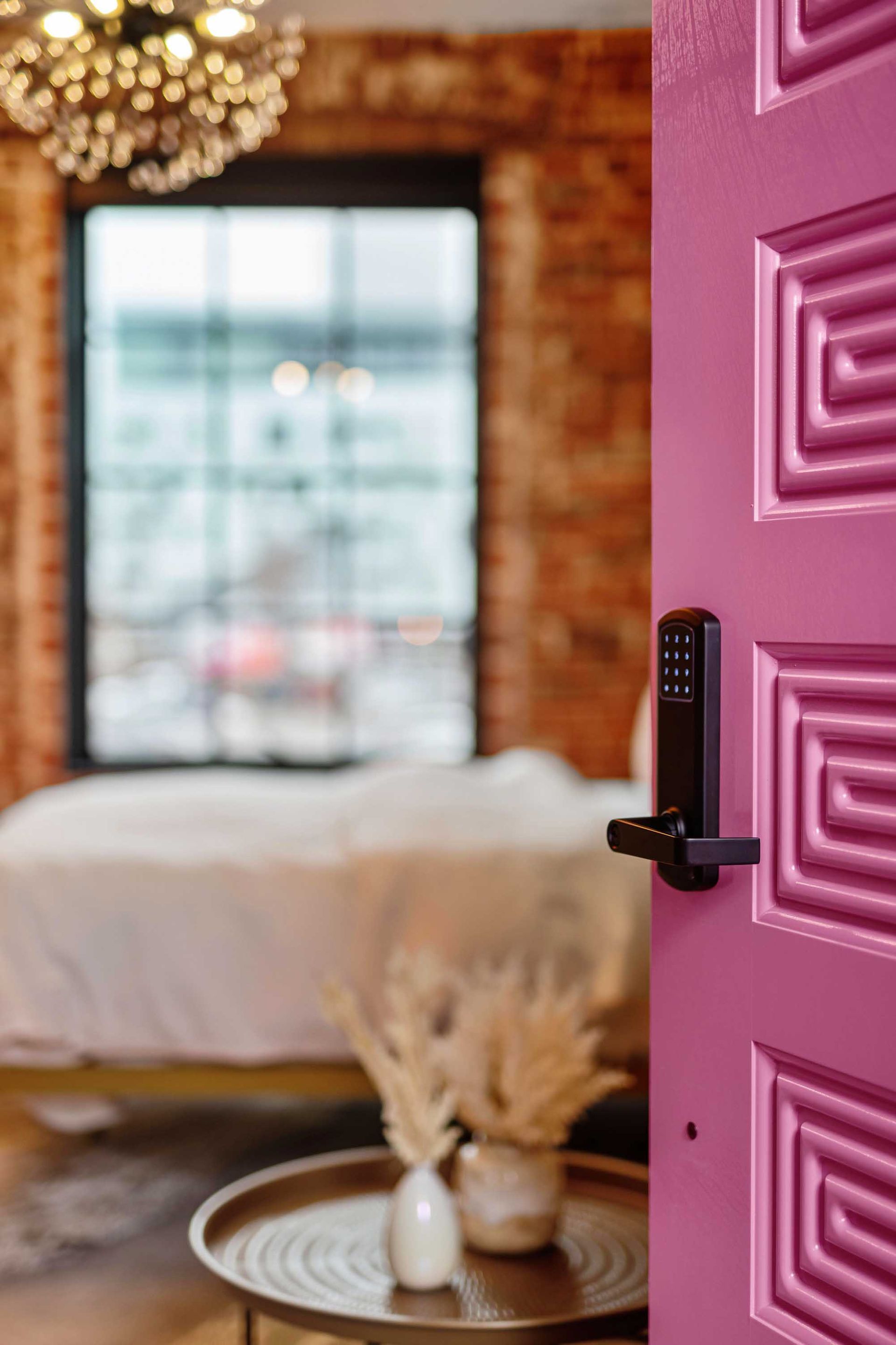 Pink front door opening into a cozy bedroom with a bed, window, and tray table.