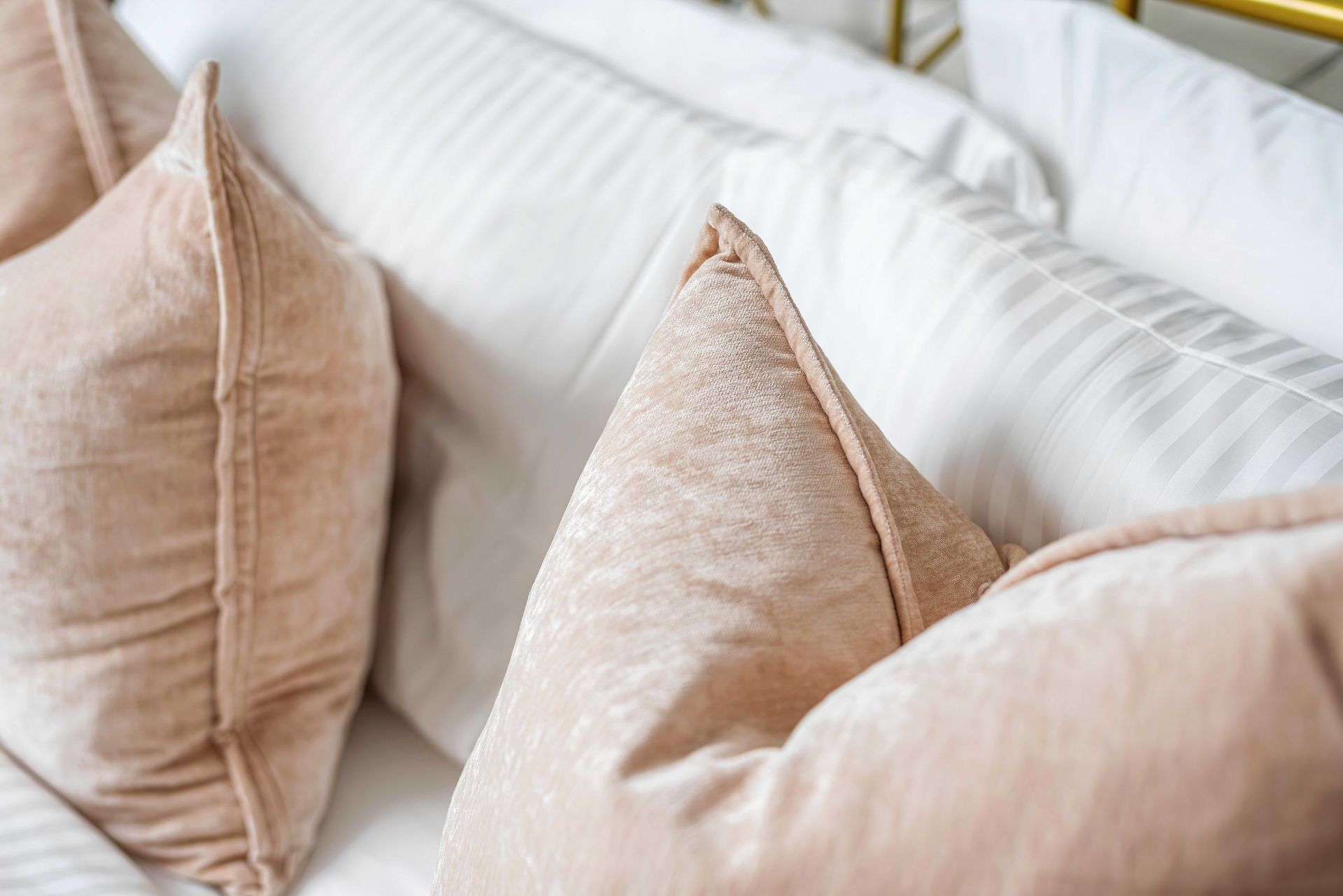 Beige throw pillows on a white bed with soft striped bedding