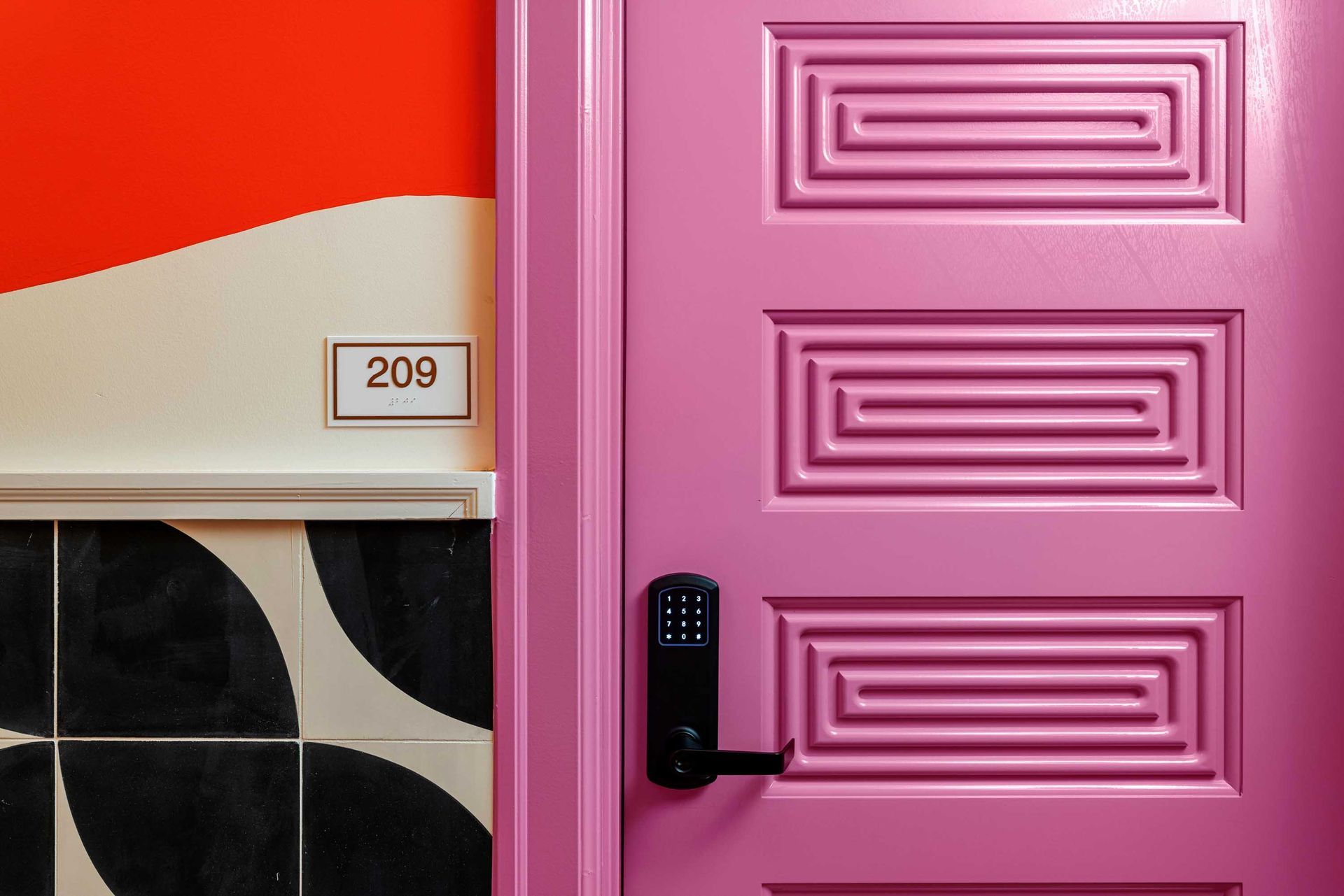 Pink front door with black handle beside a white wall marked 209 and black-and-white tile.