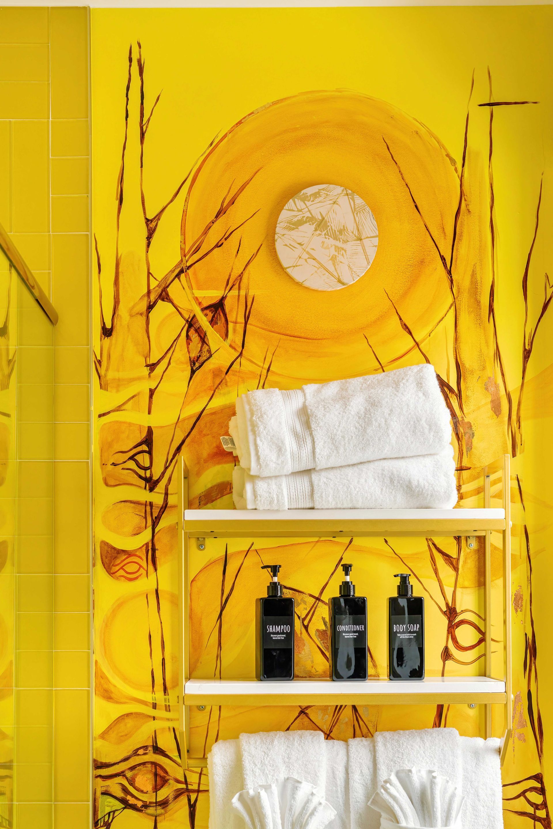 Bright yellow bathroom wall with sun mural, white towels, and a shelf holding toiletries
