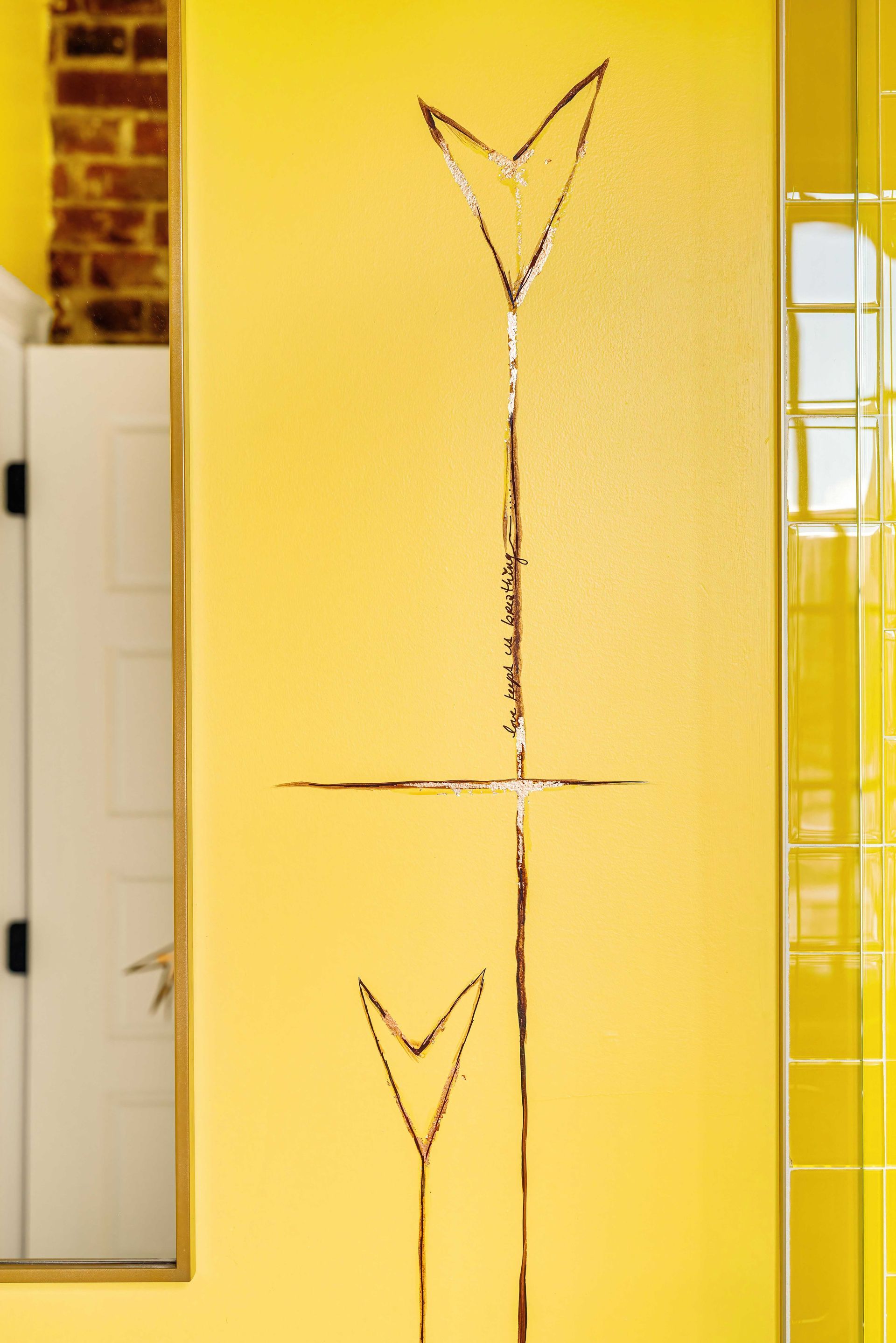 Yellow wall with two minimalist black line drawings of fork-like shapes and a horizontal line in the middle