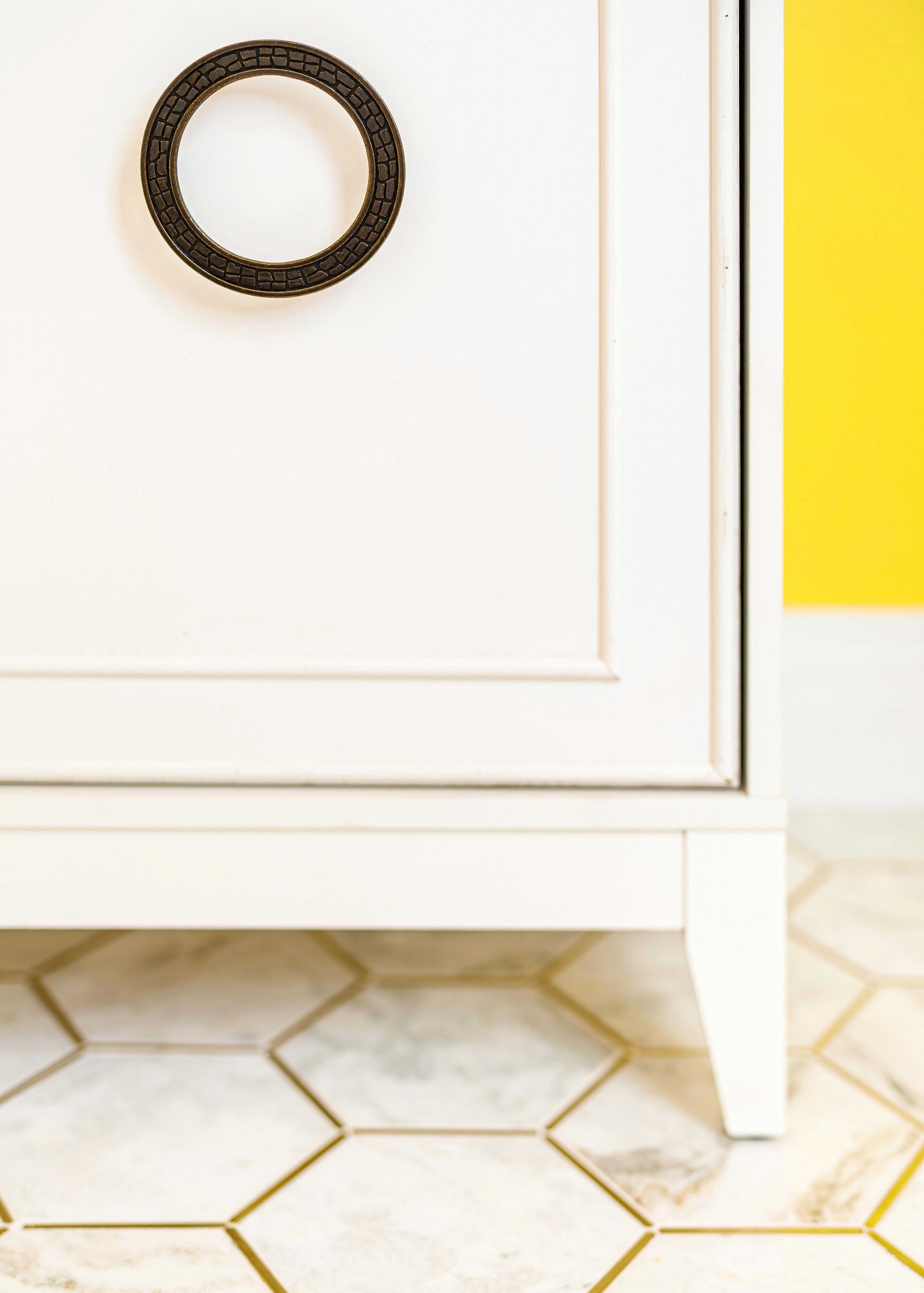 White cabinet with round black handle on hexagon tile floor, with a bright yellow wall panel nearby