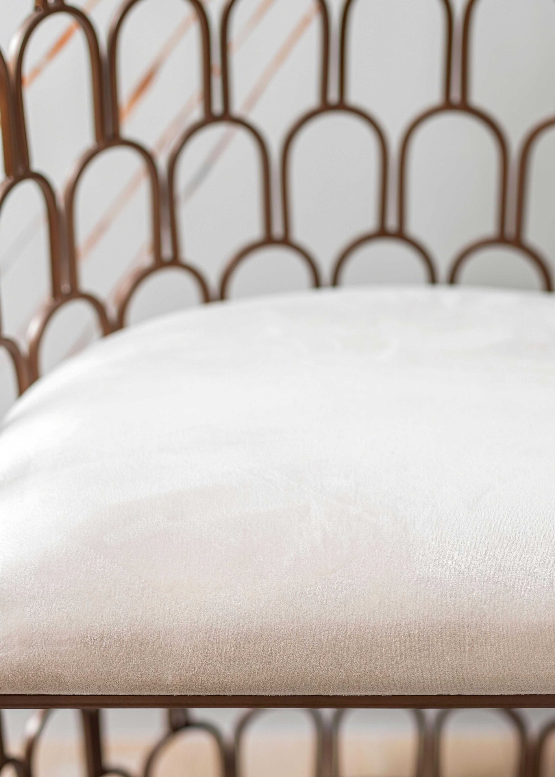 White bed pillow in front of a brown metal headboard with arched loops