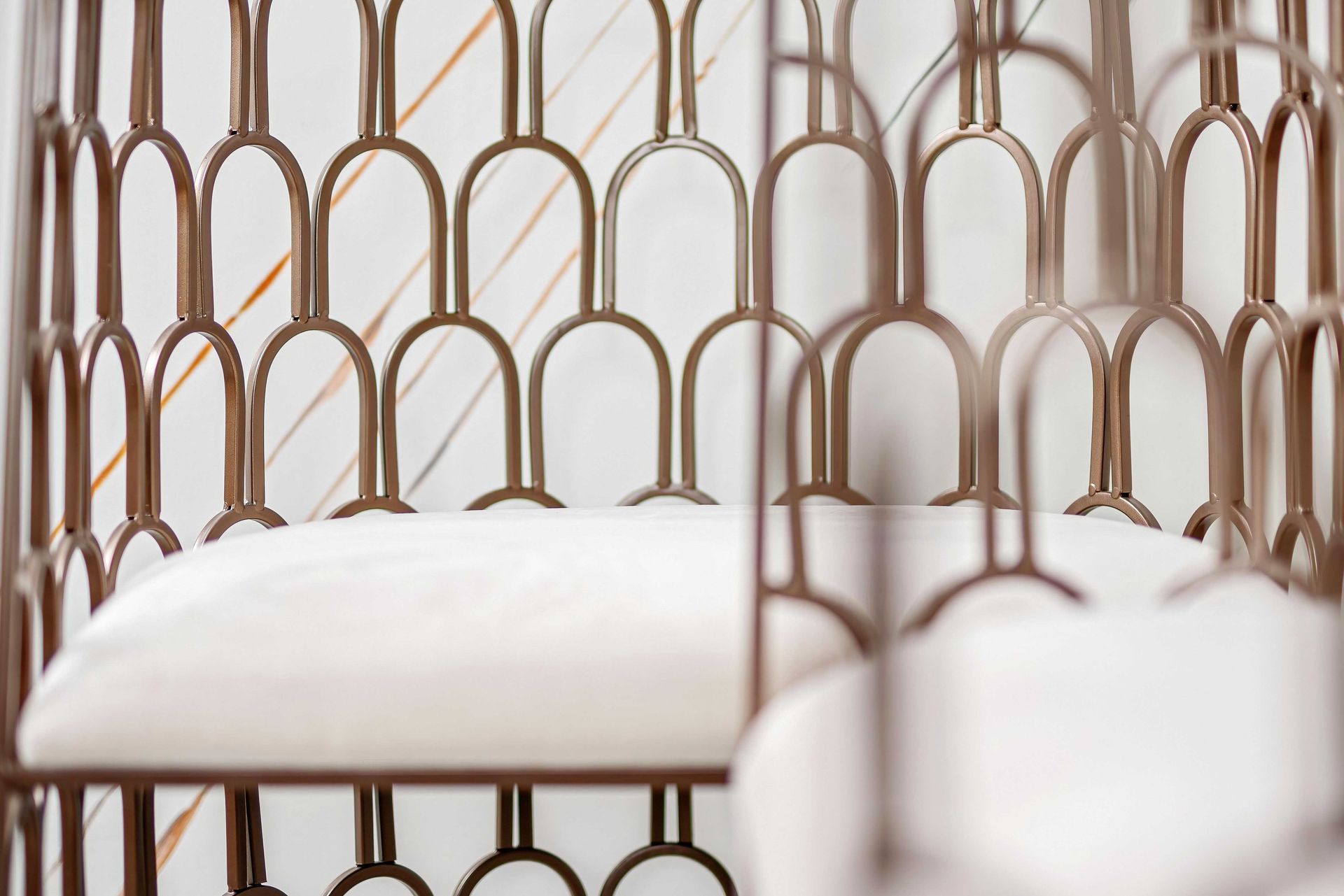 White cushions on a gold metal woven chair against a soft neutral background