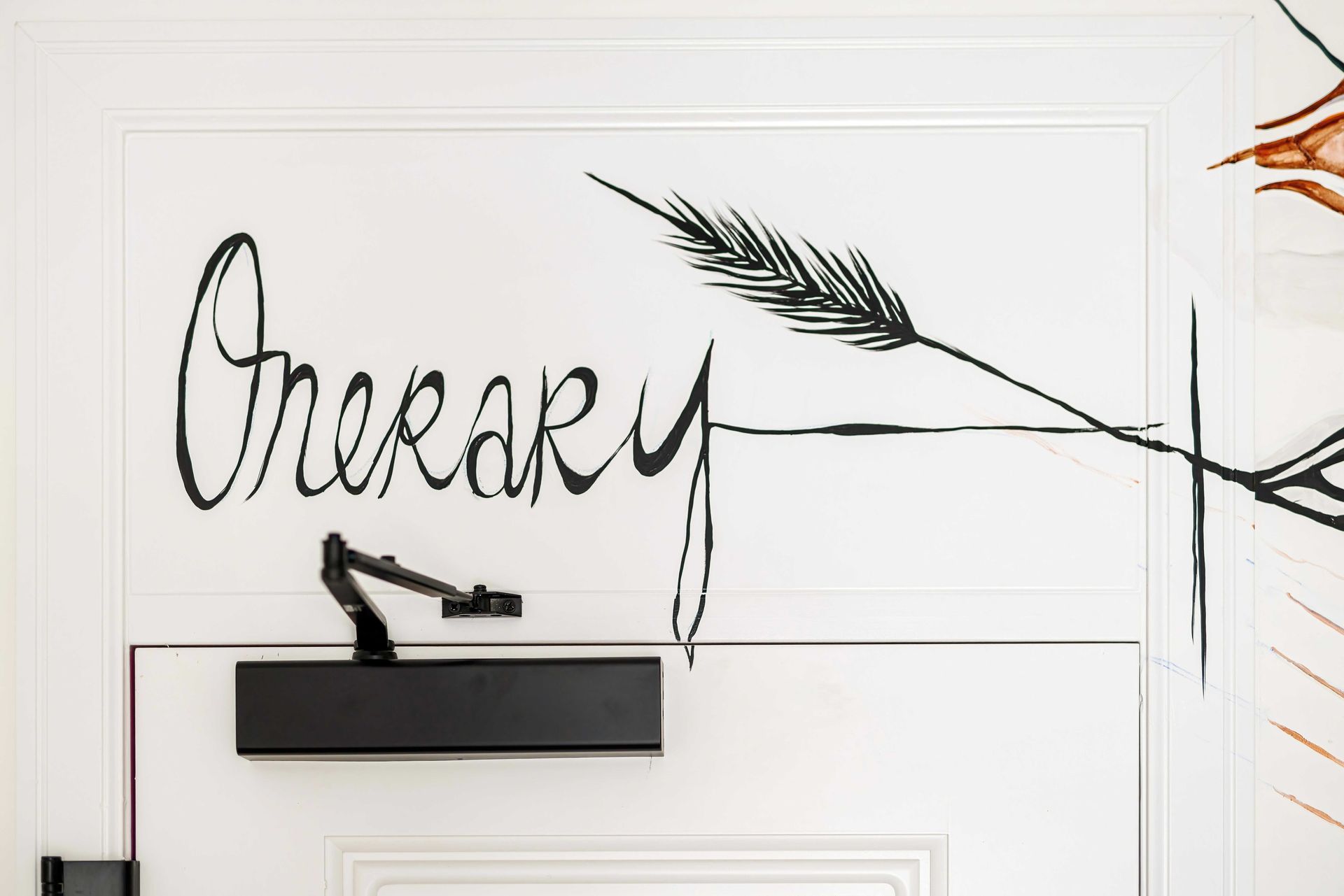 Black cursive wall art above a shelf on a white paneled wall with a leafy branch design