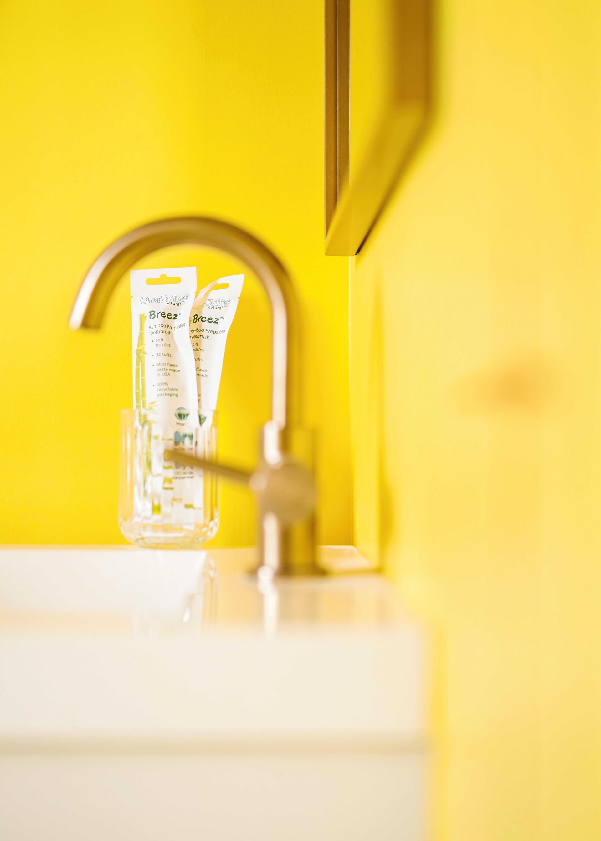 Yellow bathroom sink with faucet and white shelf holding two toothpaste tubes