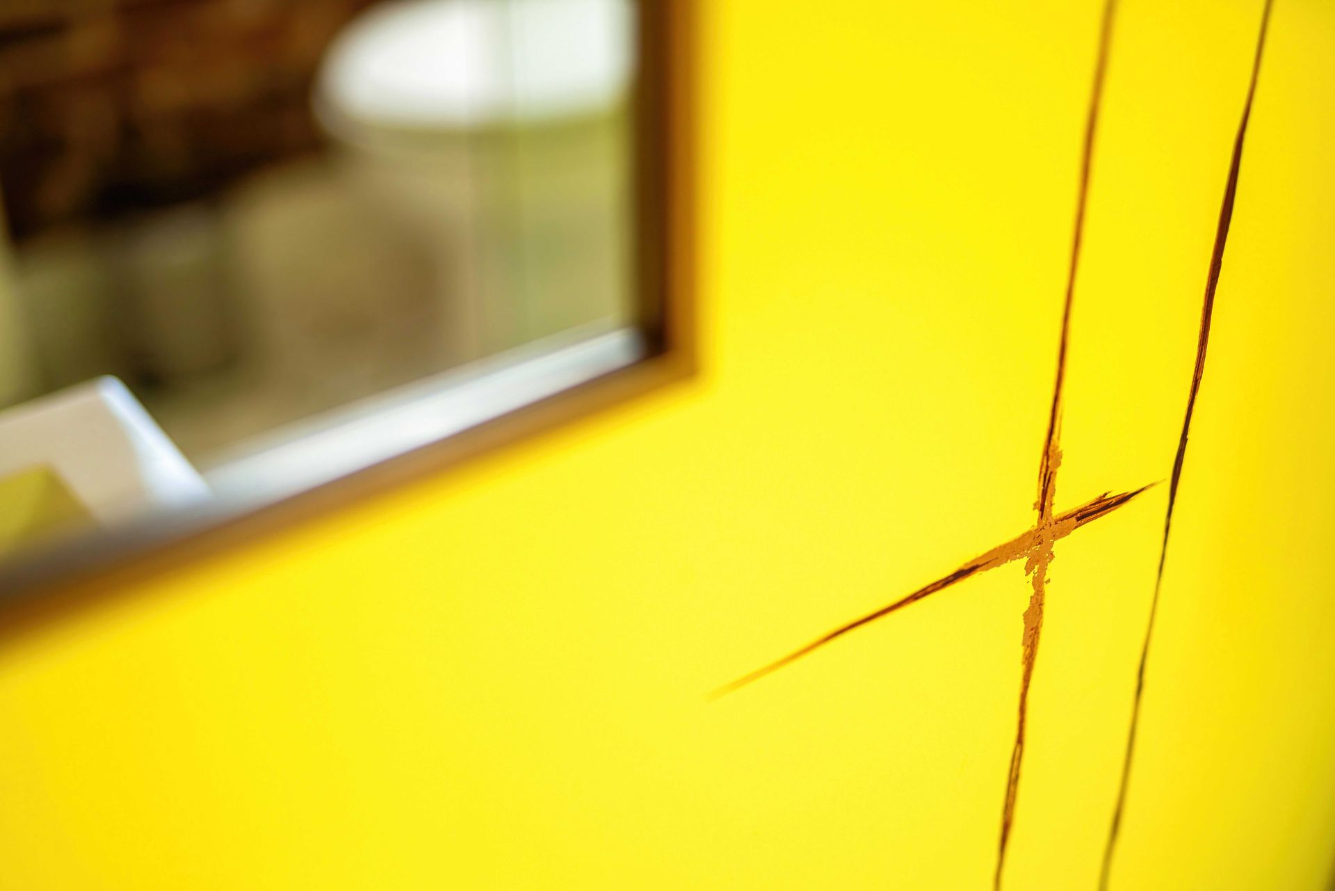 Yellow surface with a cracked or scratched area near a window reflection